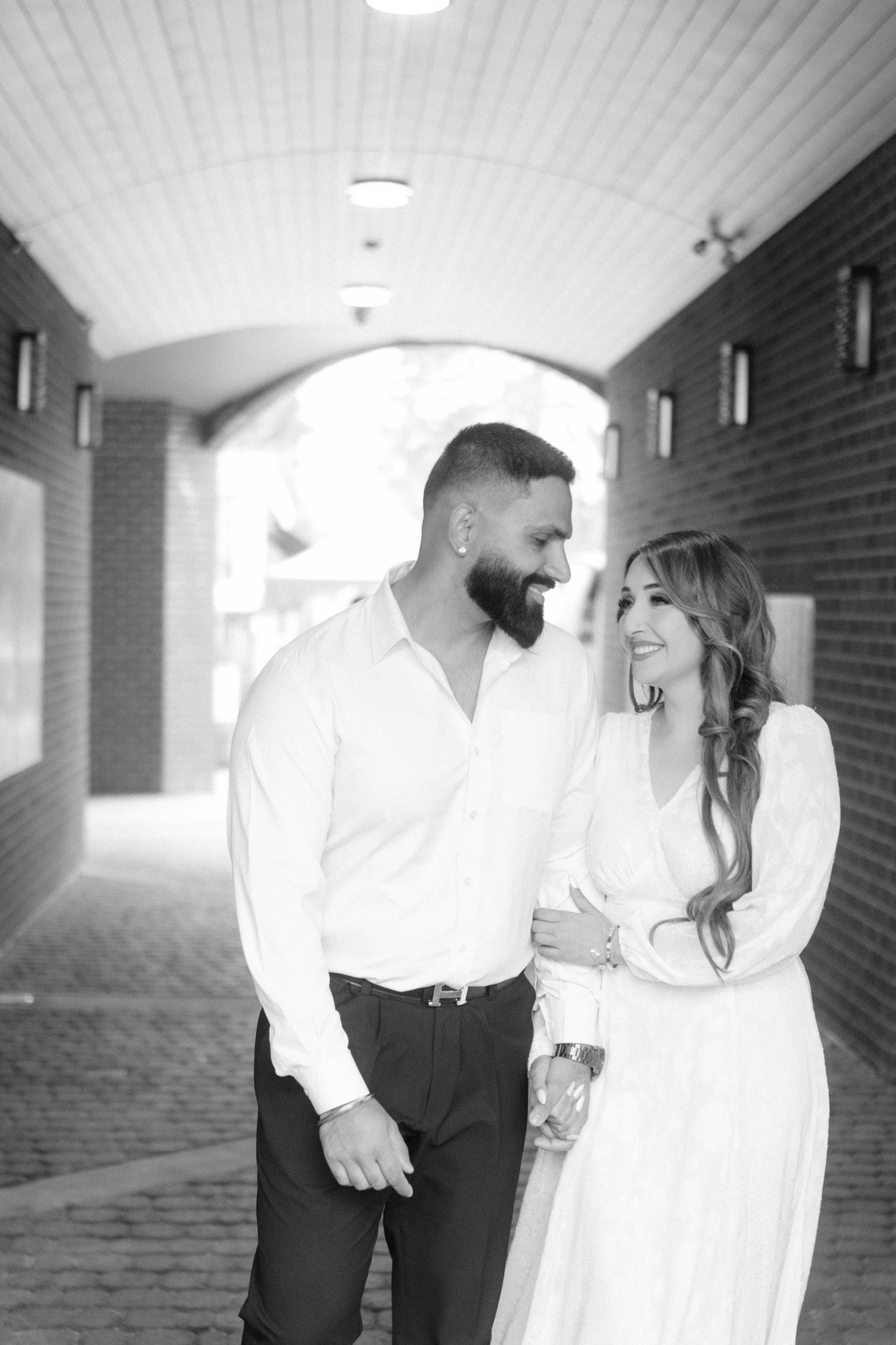 Couple shares laughter in elegant hallway wearing formal black and white attire.