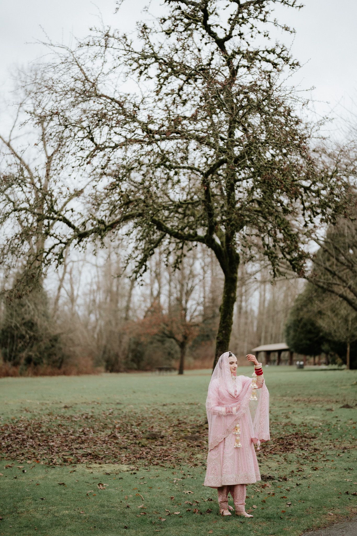 A person in a pink coat stands beneath a bare tree in a misty park setting during autumn.