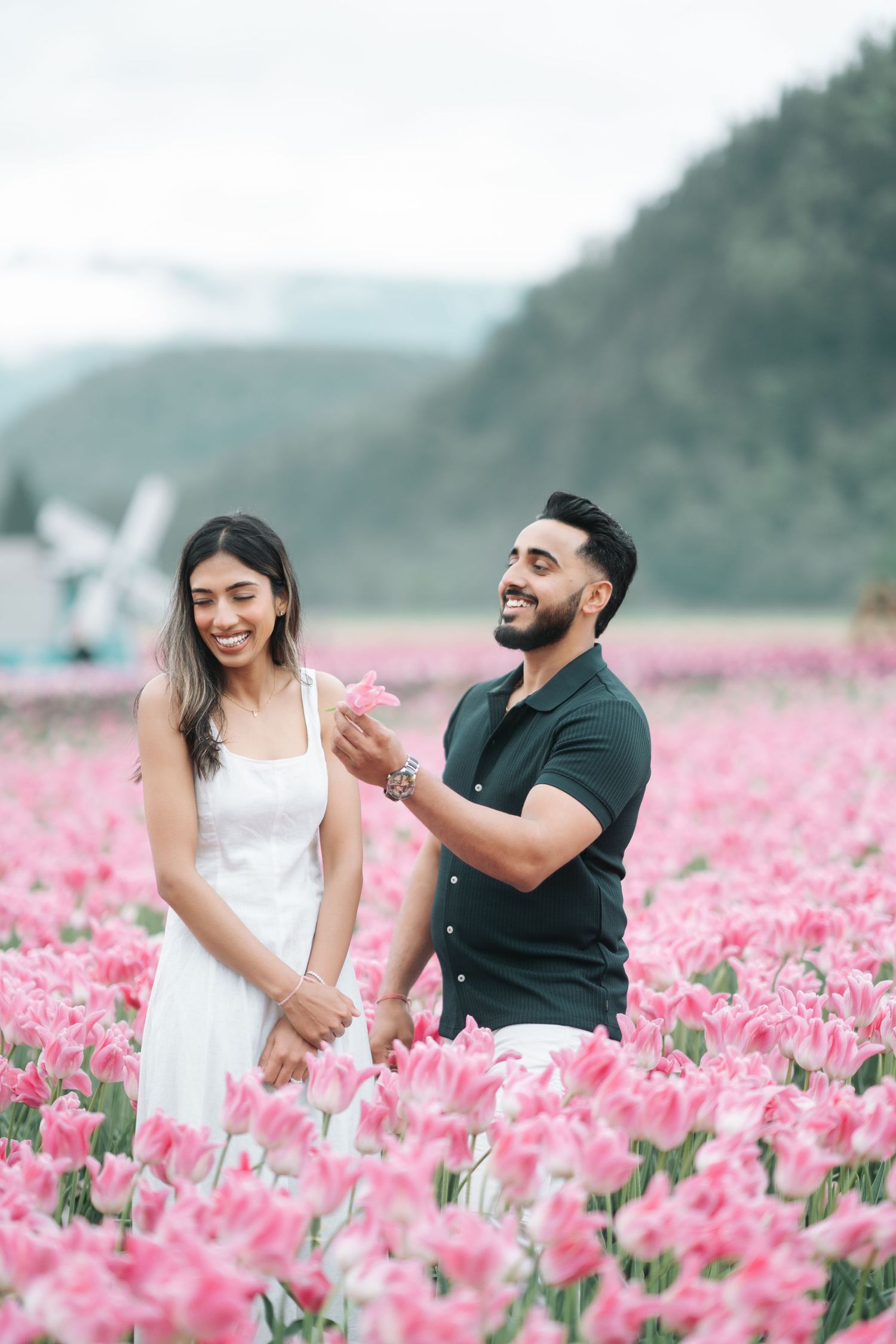 A couple shares a joyful moment together in a vibrant pink tulip field with mountains in the background.