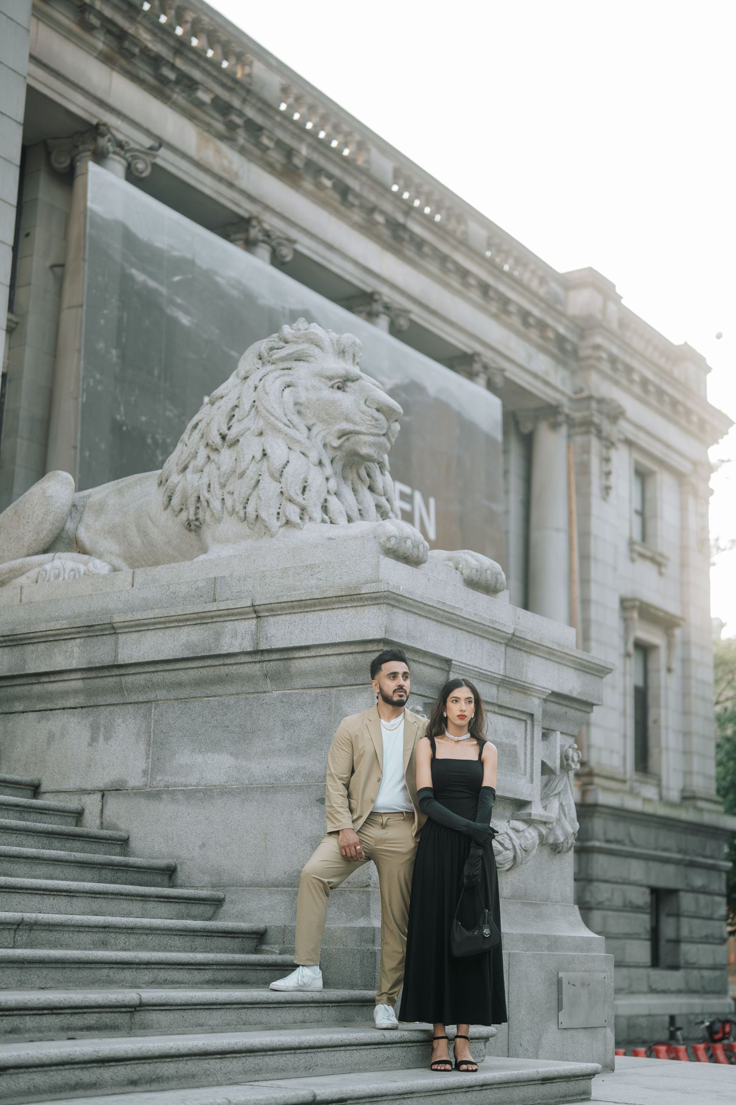 Couple sits on grand stone steps of historic building with ornate lion sculptures and architectural details.