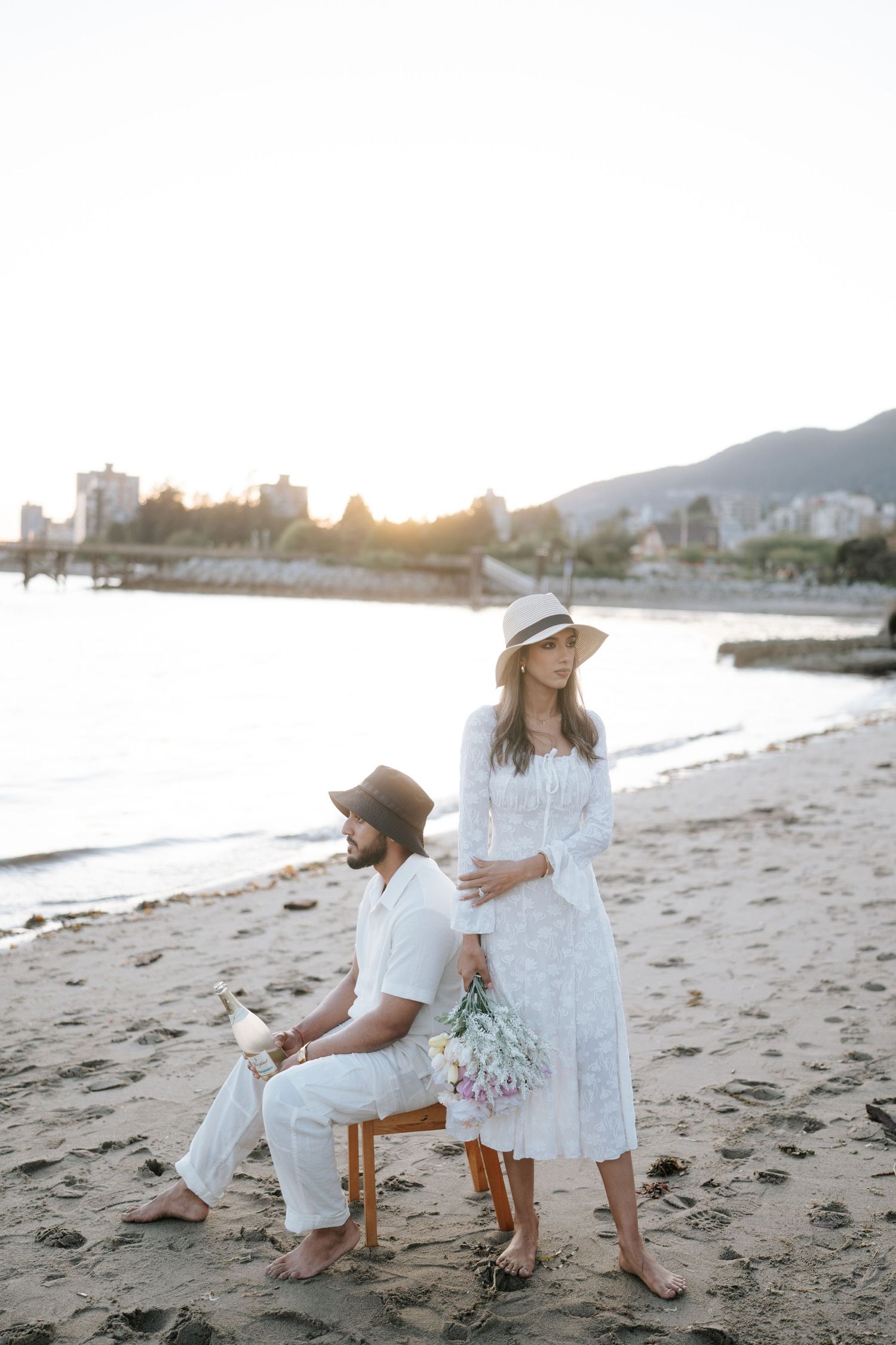 Family in white outfits playing together on a sandy beach at sunset with mountains in the background.