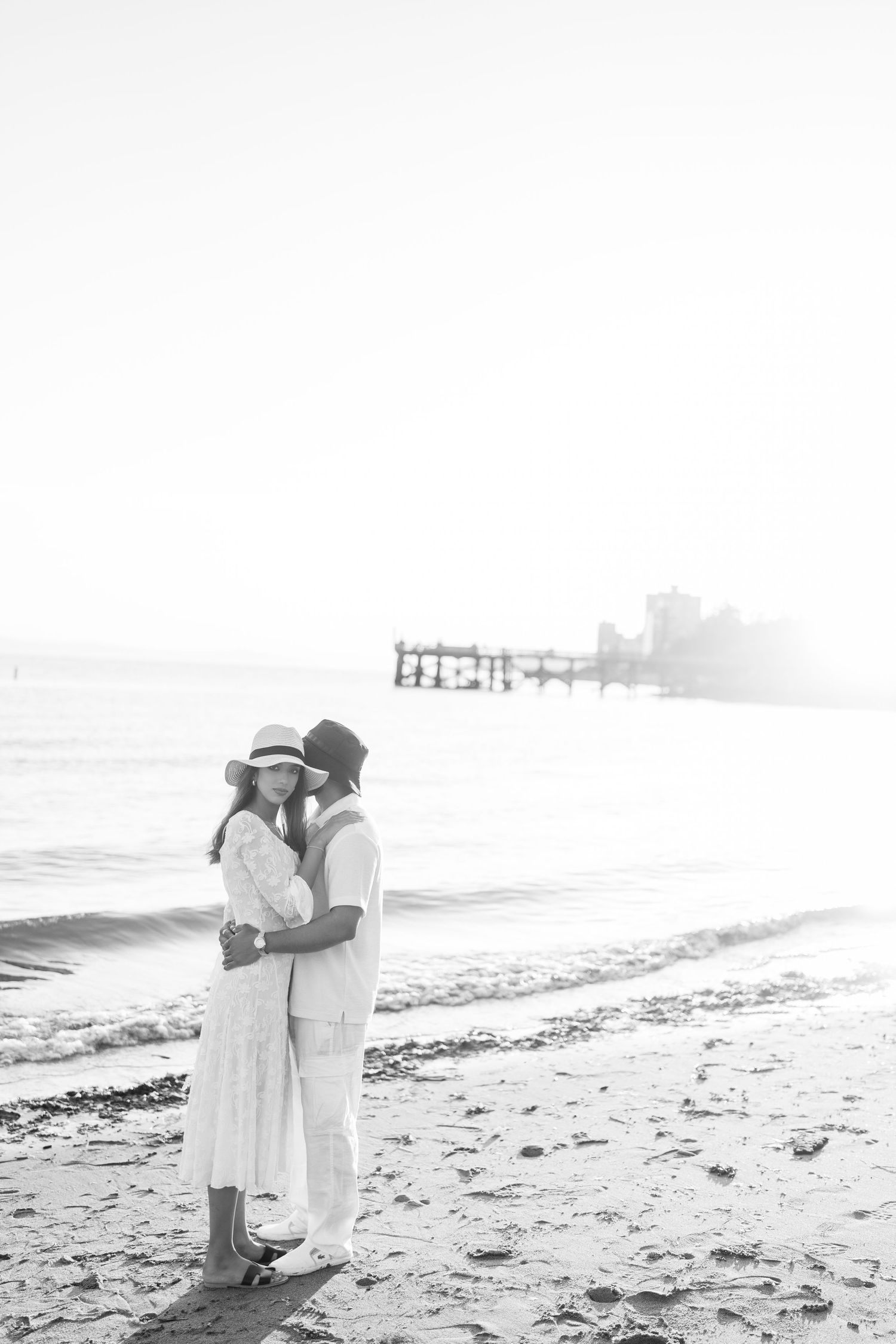 A romantic black and white photo series of a couple embracing on a misty beach at sunset.
