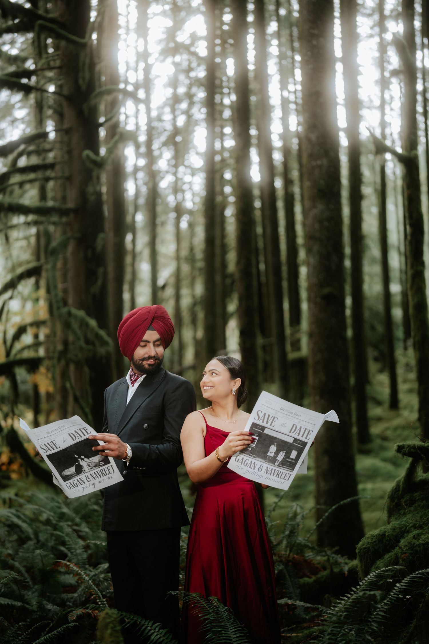 A couple reads save-the-date newspapers while standing in a misty forest setting.