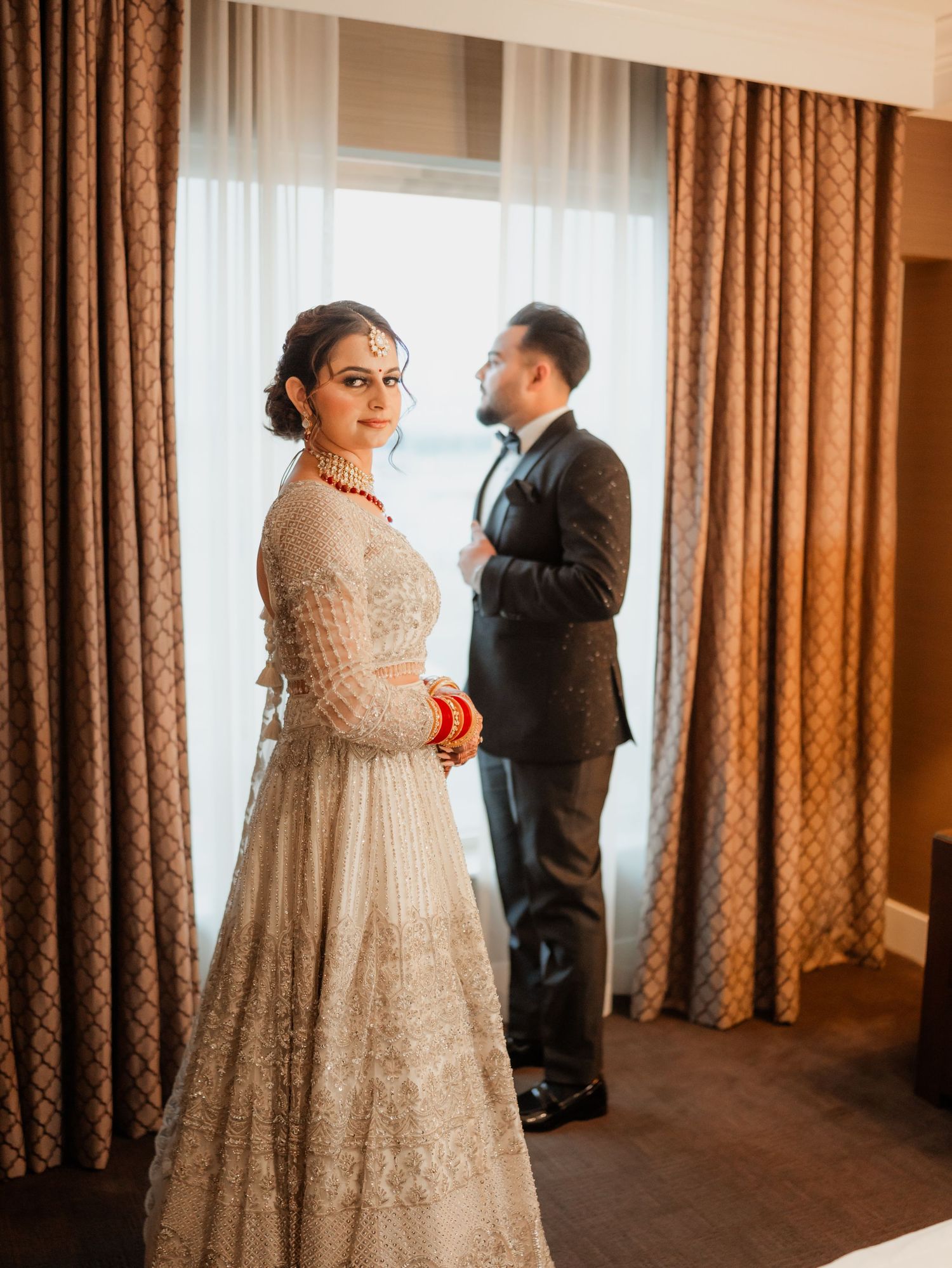A romantic scene between two people in formal attire standing near elegant brown drapes.