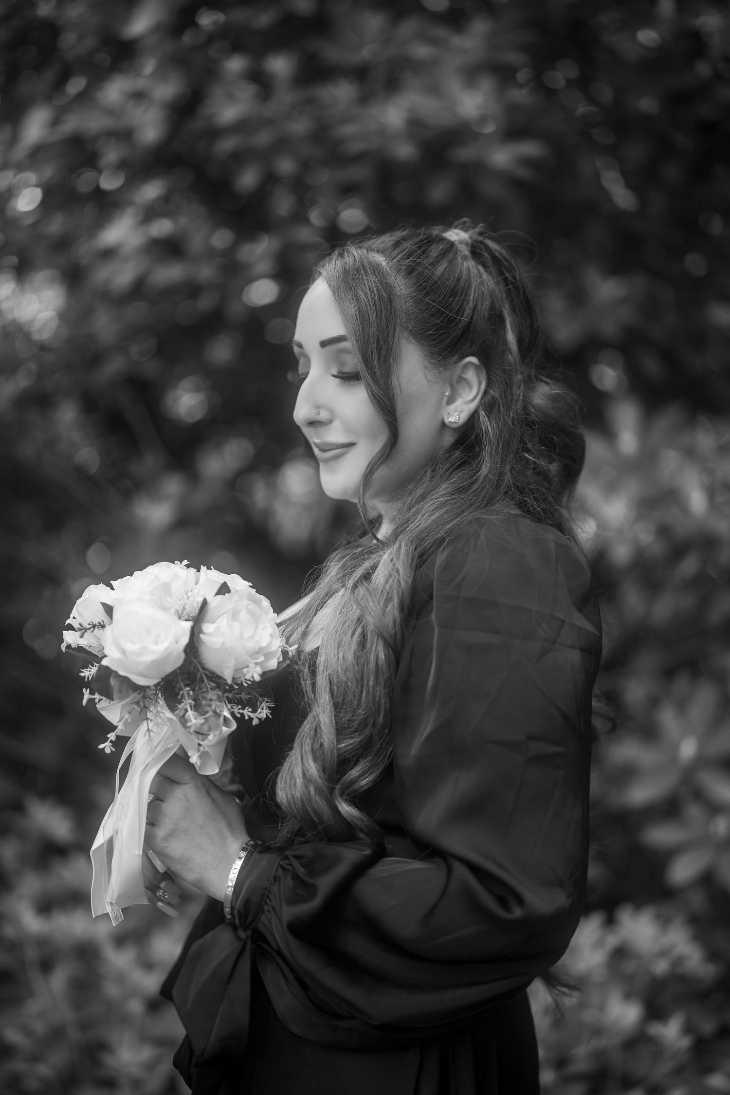 Black and white portrait of a young woman holding a bouquet of roses, smiling softly outdoors.