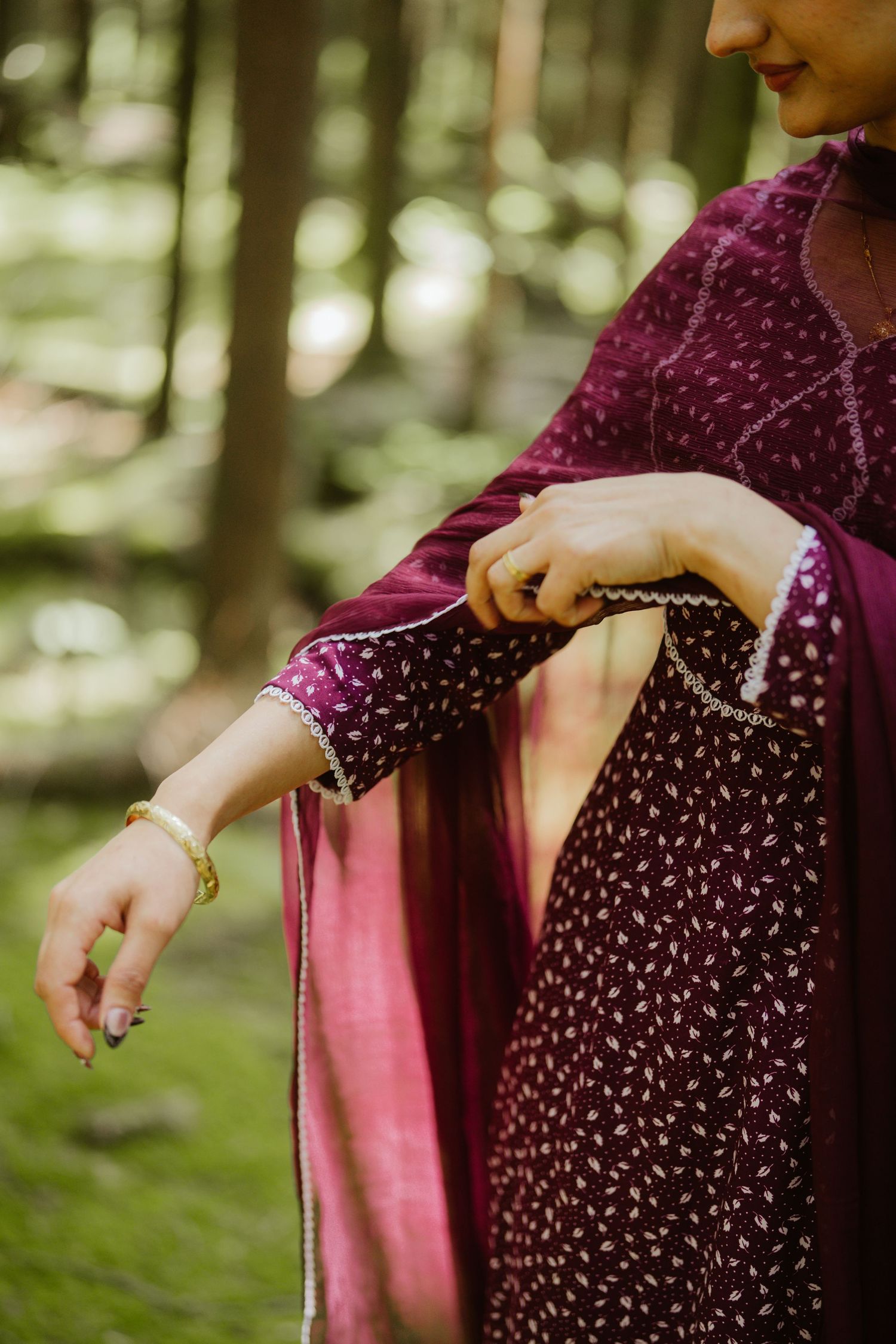 Close-up of a woman adjusting her burgundy embroidered salwar kameez sleeve in a forest.