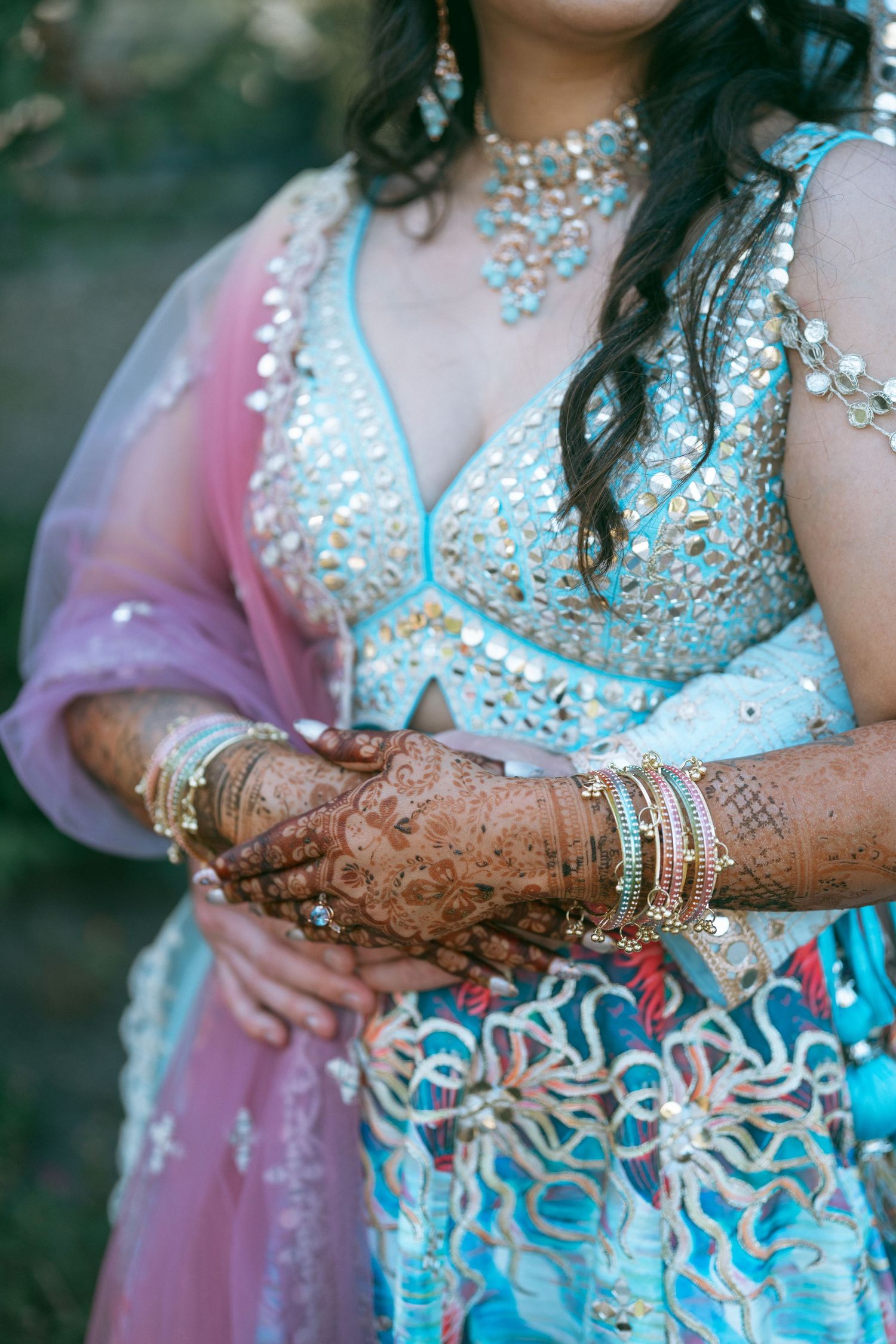 Indian bride in blue lehenga with henna mehndi hands, gold bangles, and turquoise jewelry at wedding ceremony.