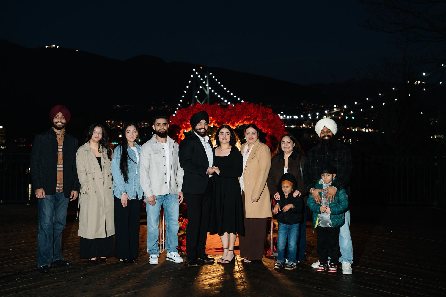A group of people standing on a pier at night with illuminated string lights in the background.