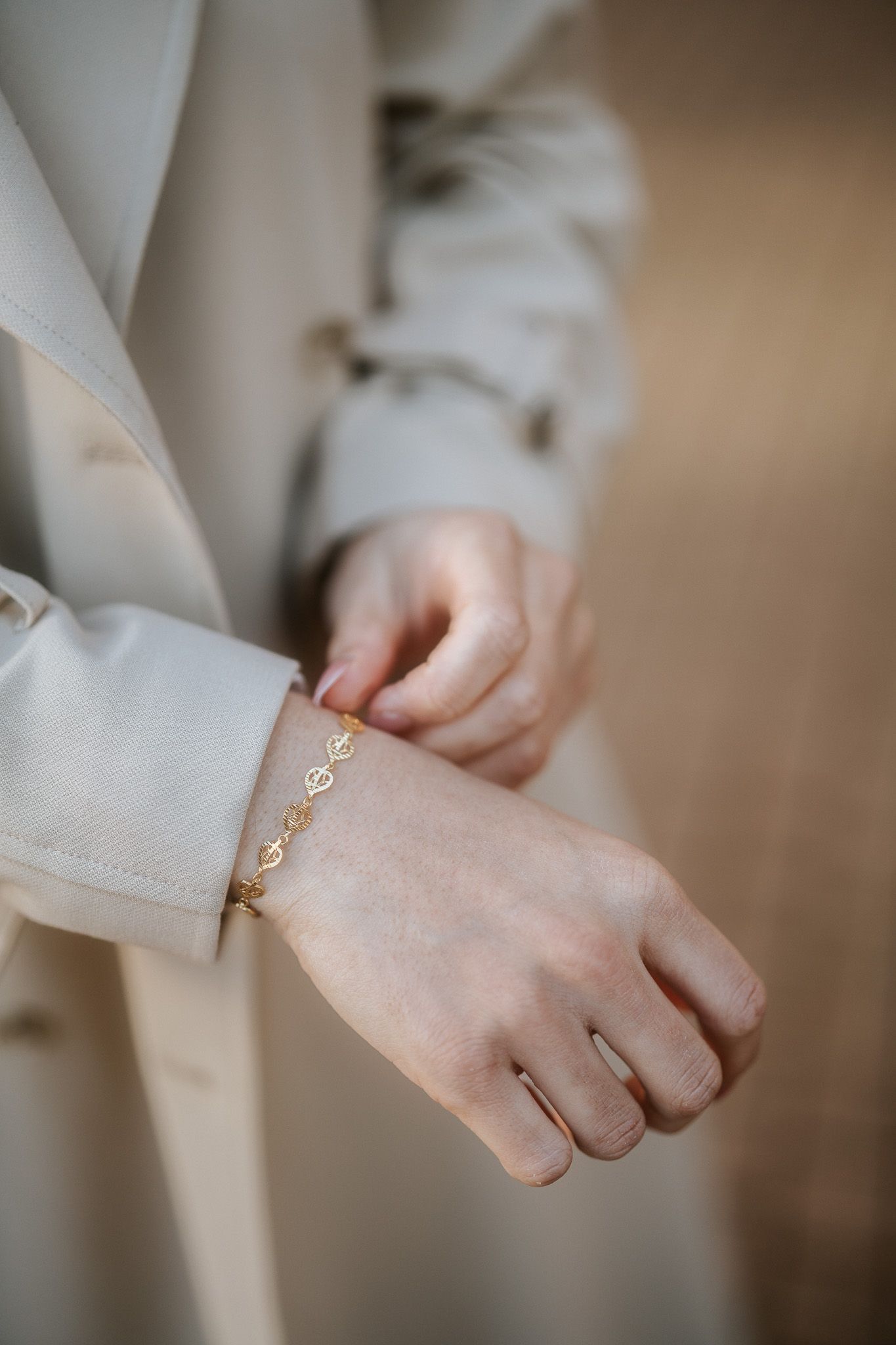 Close-up view of hands fastening a delicate gold chain bracelet against light beige clothing.