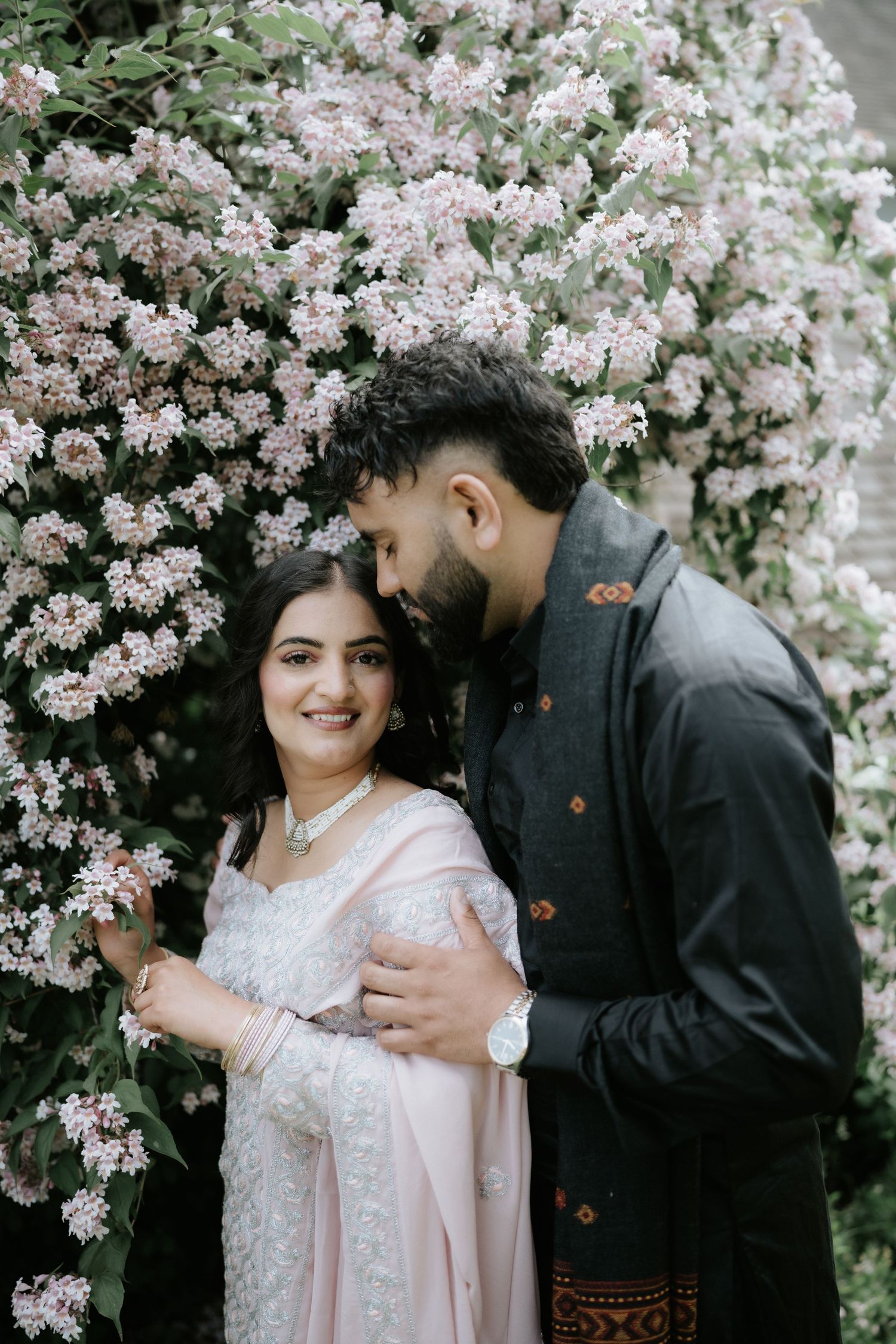 A couple poses romantically under flowering cherry blossoms in spring.