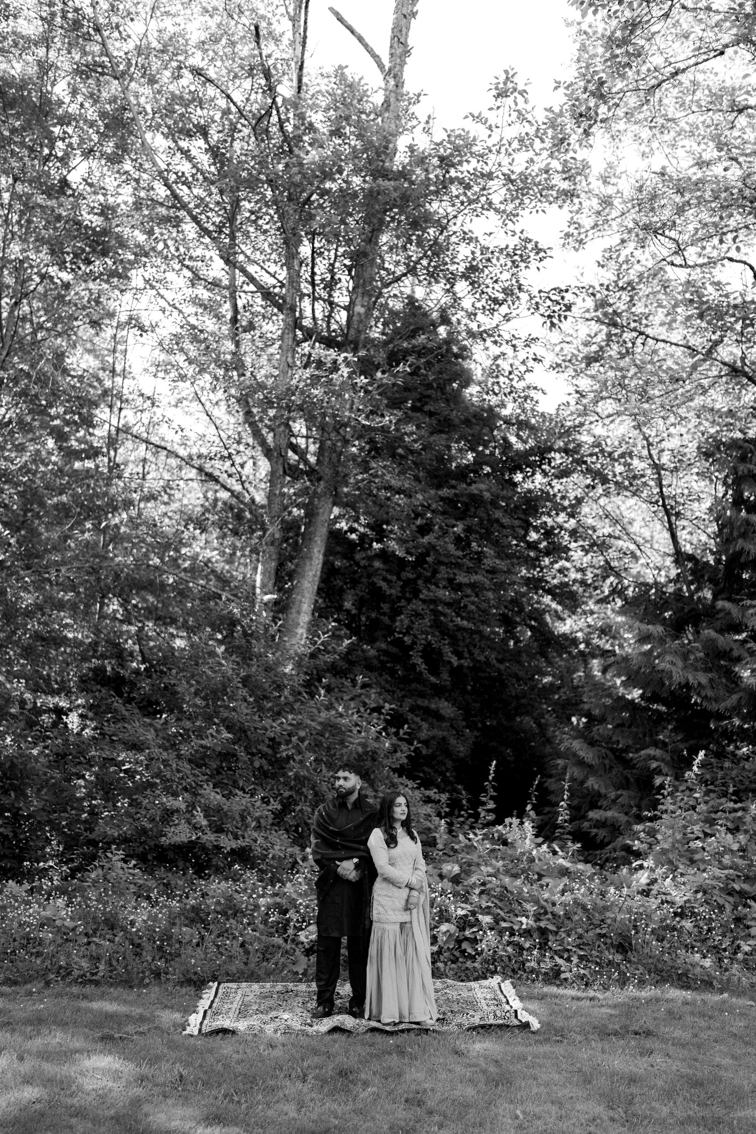 Black and white photo of two figures standing among trees in a natural outdoor setting.