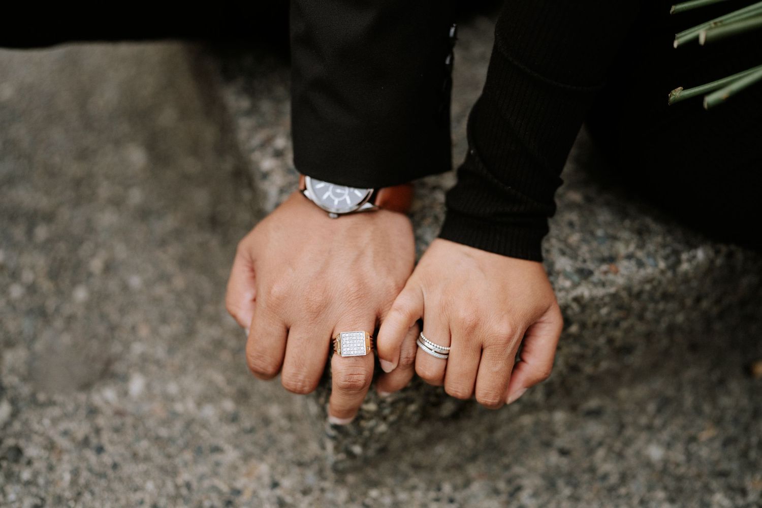 Two hands with rings rest together on a textured stone surface.