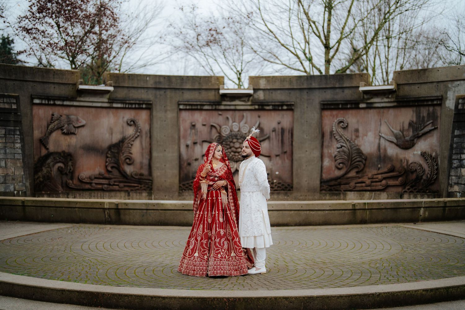 Outdoor wedding photoshoot in front of a stone wall structure on a cloudy day.