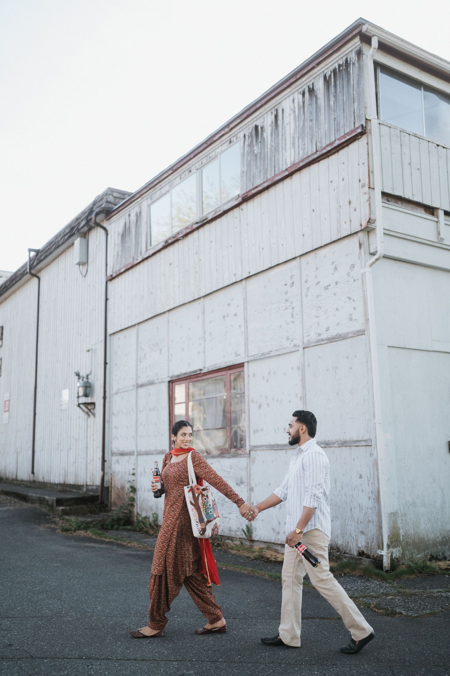 Two people dance and pose playfully in front of a rustic white barn wall in a sequence of five connected photos.