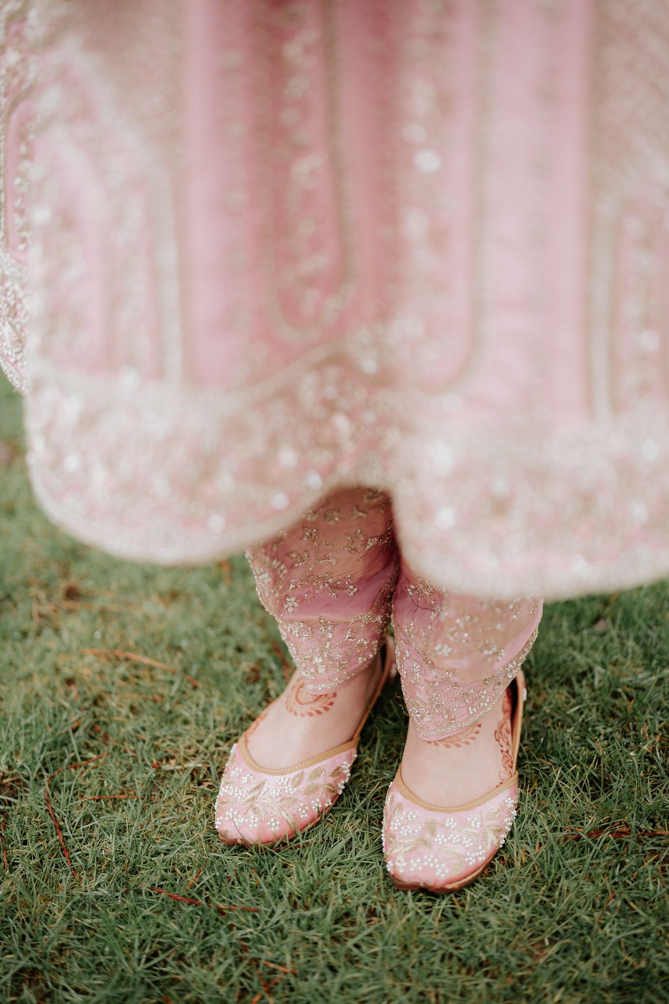 Close-up view of pink glittery shoes on grass with a flowing pink dress hem visible.