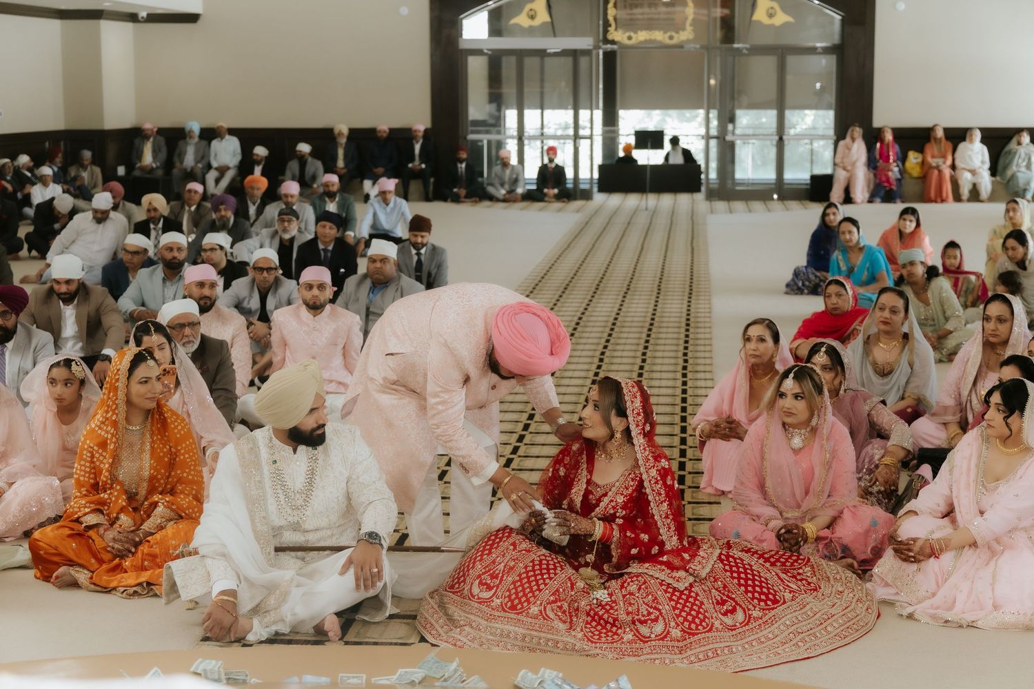 Sikh wedding ceremony with bride in red lehenga and guests seated on floor in a gurudwara.