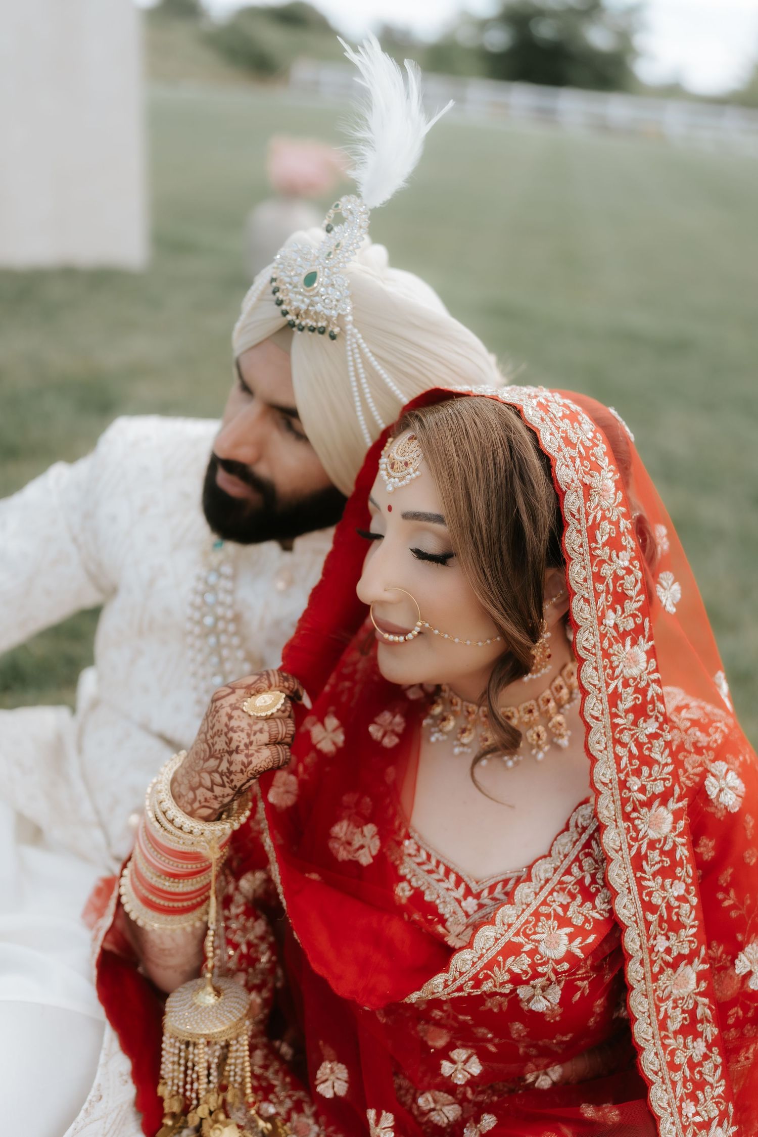 Sikh bride in red embroidered lehenga and groom in white sherwani and turban sharing a joyful wedding moment.