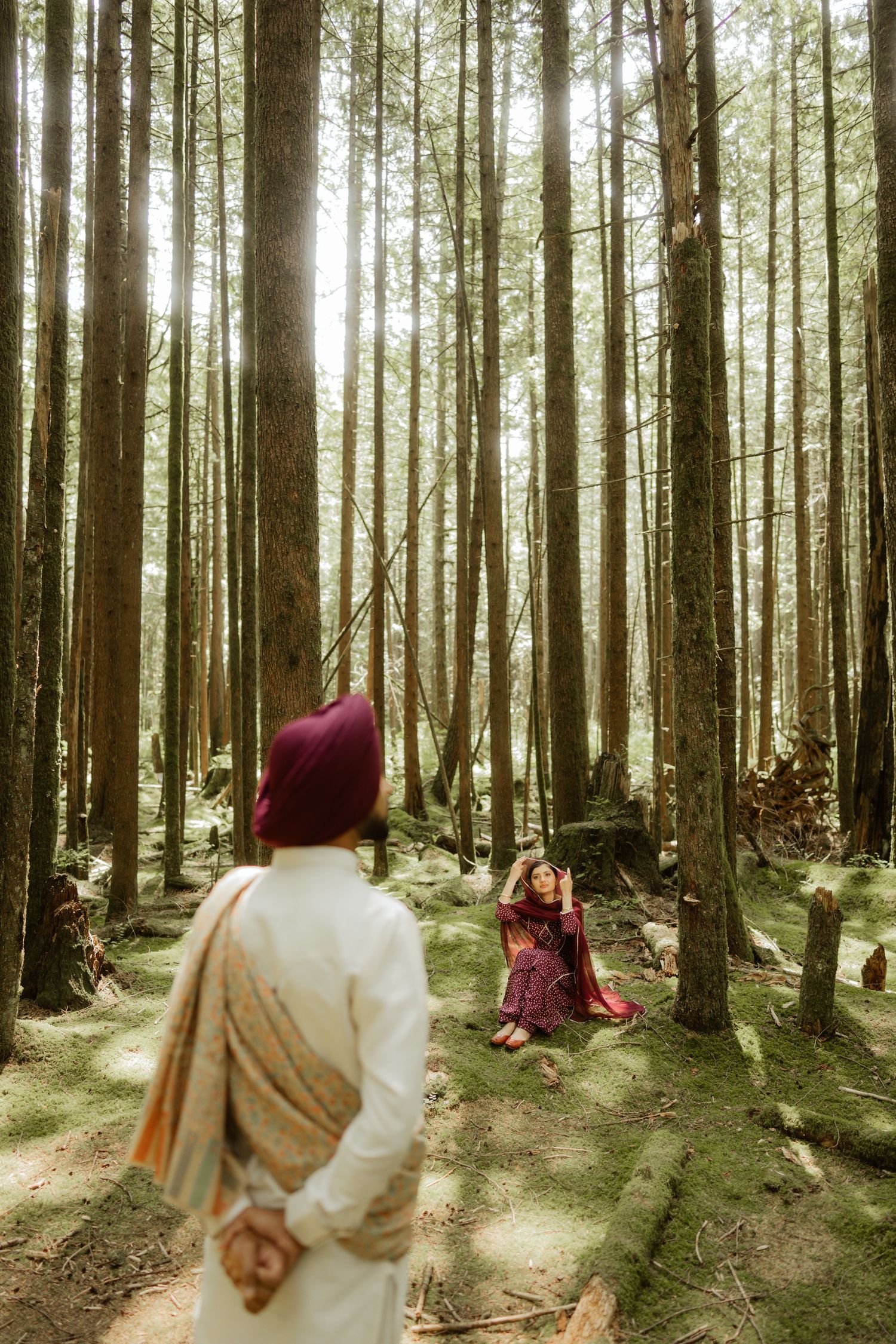Sikh couple in traditional attire sharing a romantic first look moment in a sunlit forest.