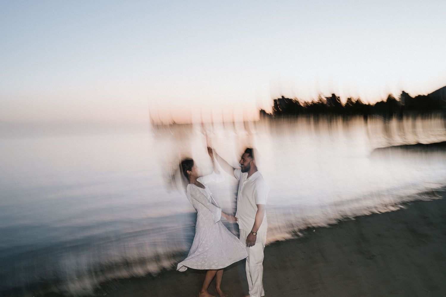A dreamy series of blurred motion photographs showing someone in white walking along a misty beach at sunset.