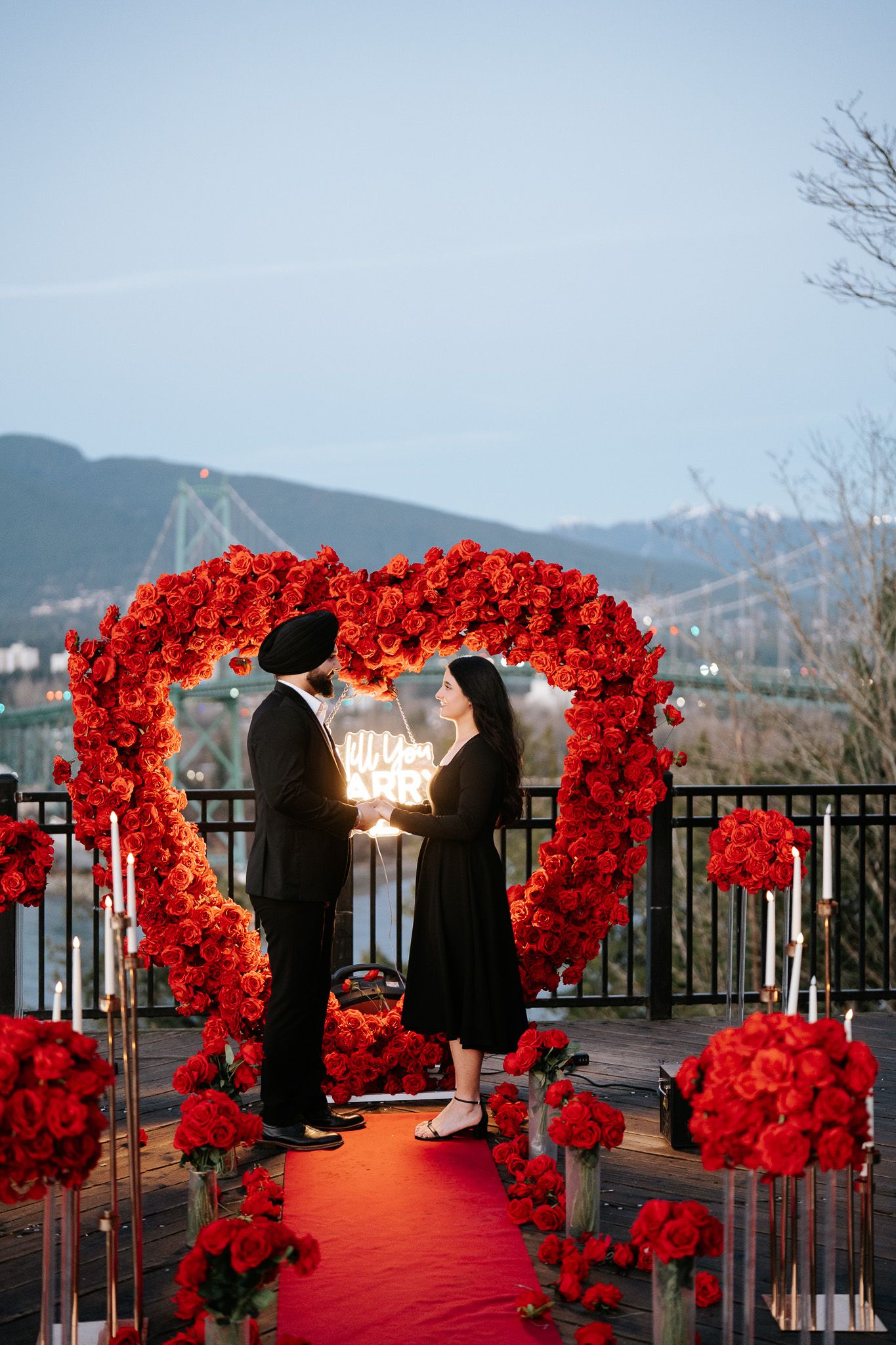 Red floral archways line a walkway with mountain views at a romantic outdoor wedding venue at sunset.