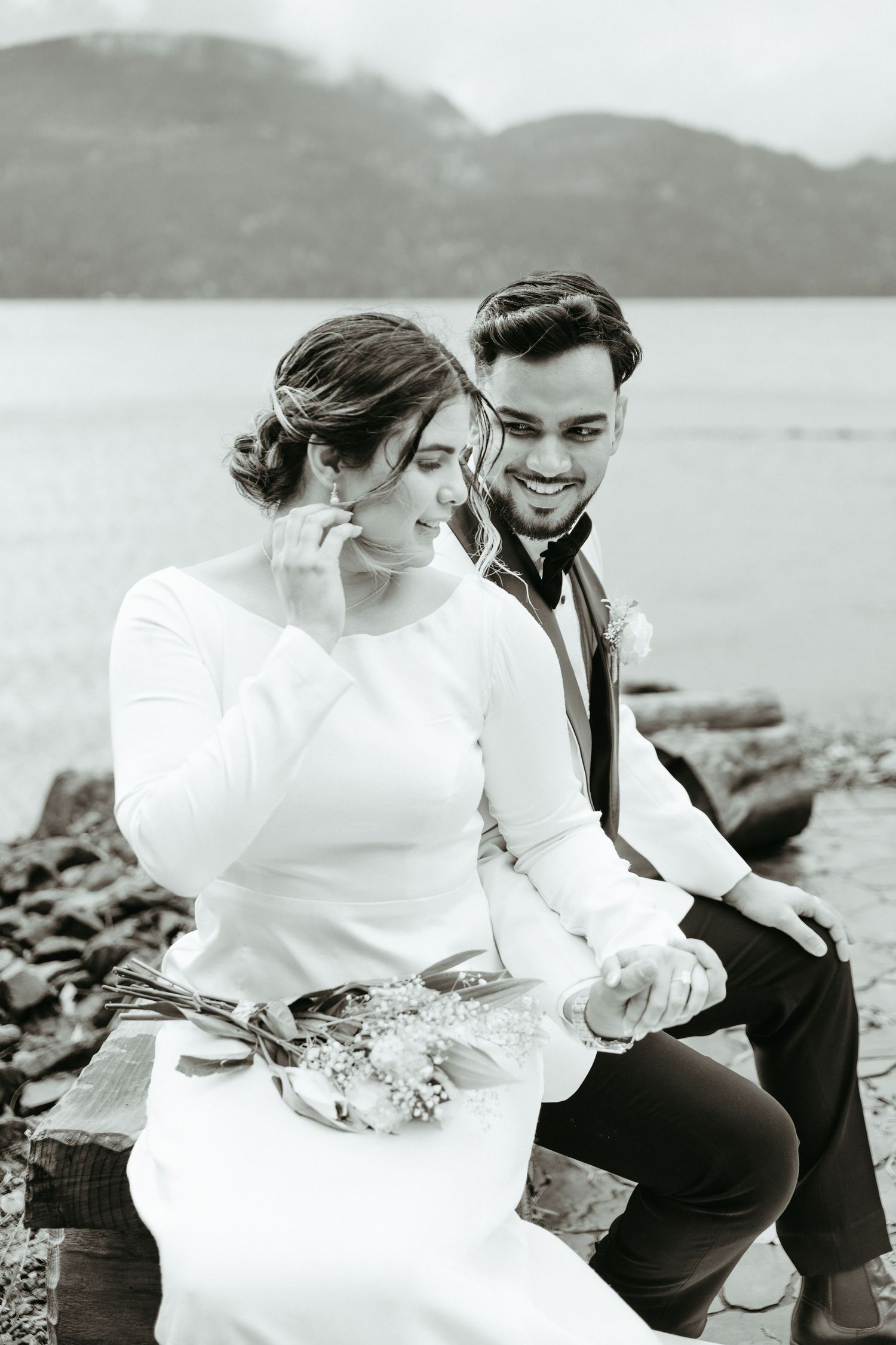 A couple sits together on rocky coastal terrain in black and white vintage-style wedding photos.
