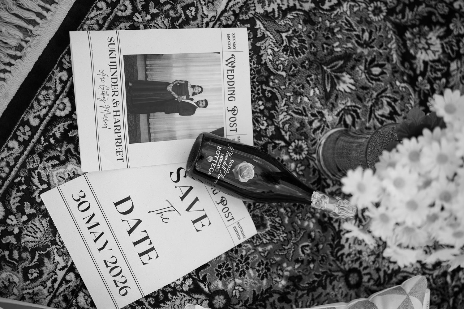 Black and white flat lay of save the date cards, wedding magazine, champagne bottle and flowers.