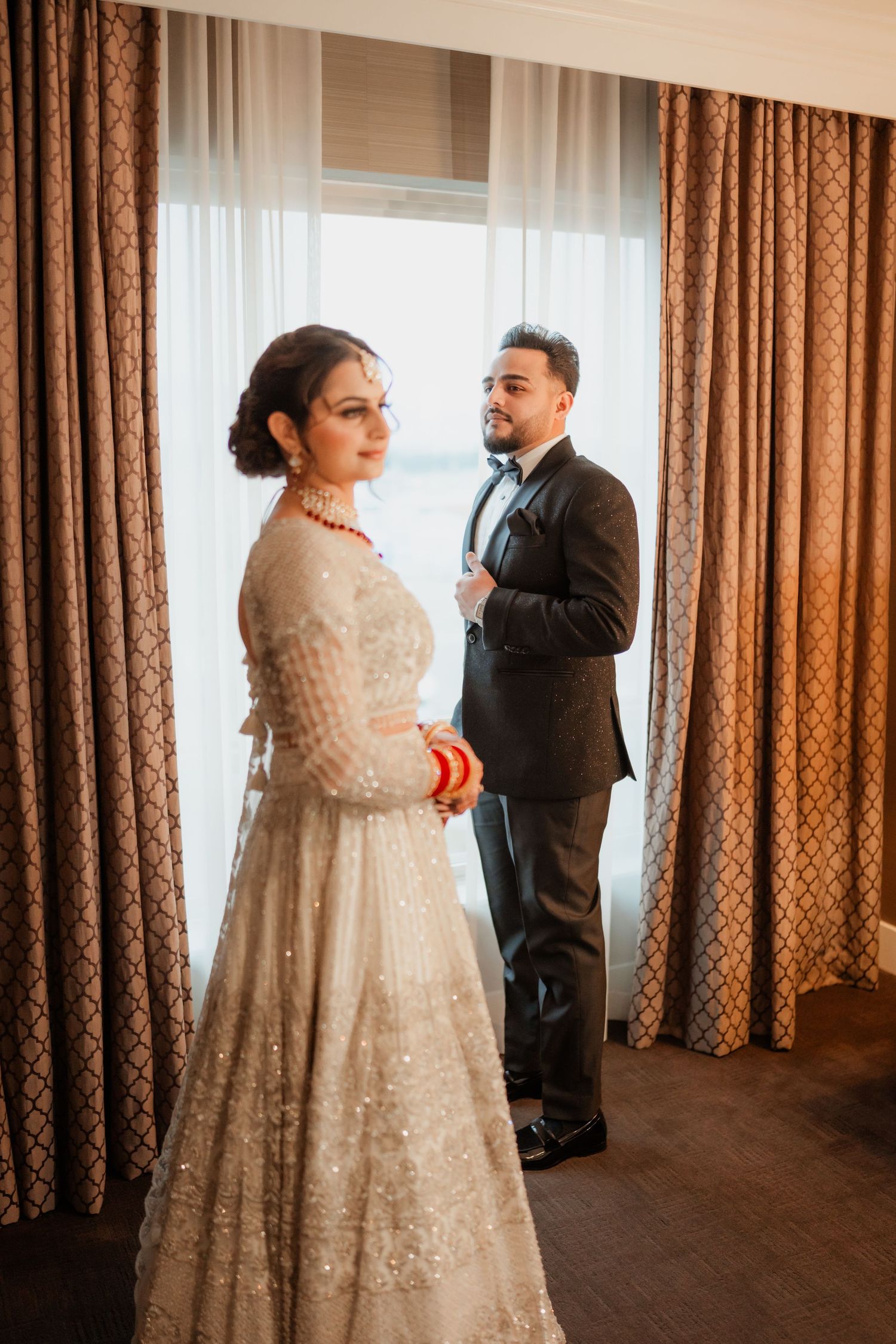 A couple shares an intimate moment in a hotel room with brown curtains and soft lighting.