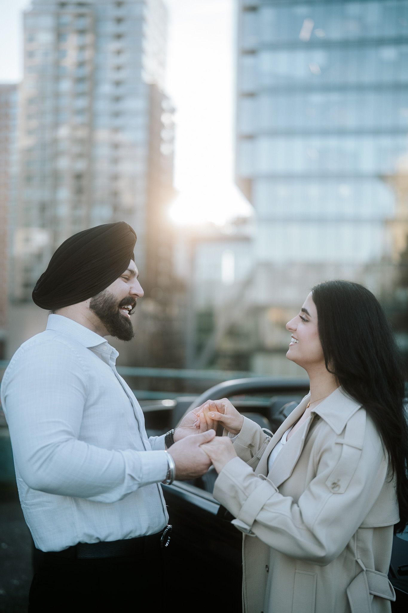 A couple in white outfits playfully interact in front of a modern building during sunset.