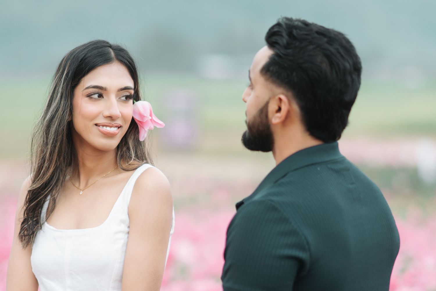 Couple in formal attire poses romantically in a blooming pink flower garden during a photoshoot.