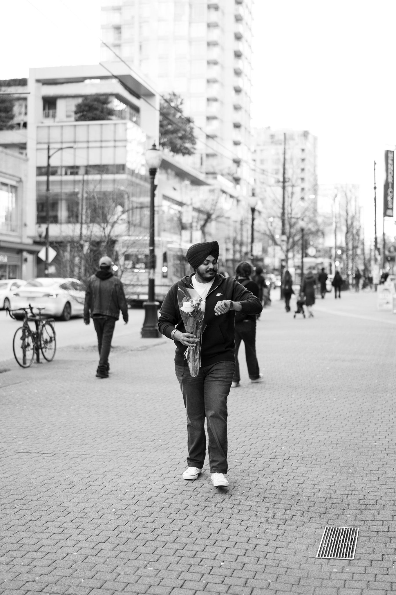 Black and white street photography of a pedestrian walking on a brick sidewalk in an urban area with tall buildings.