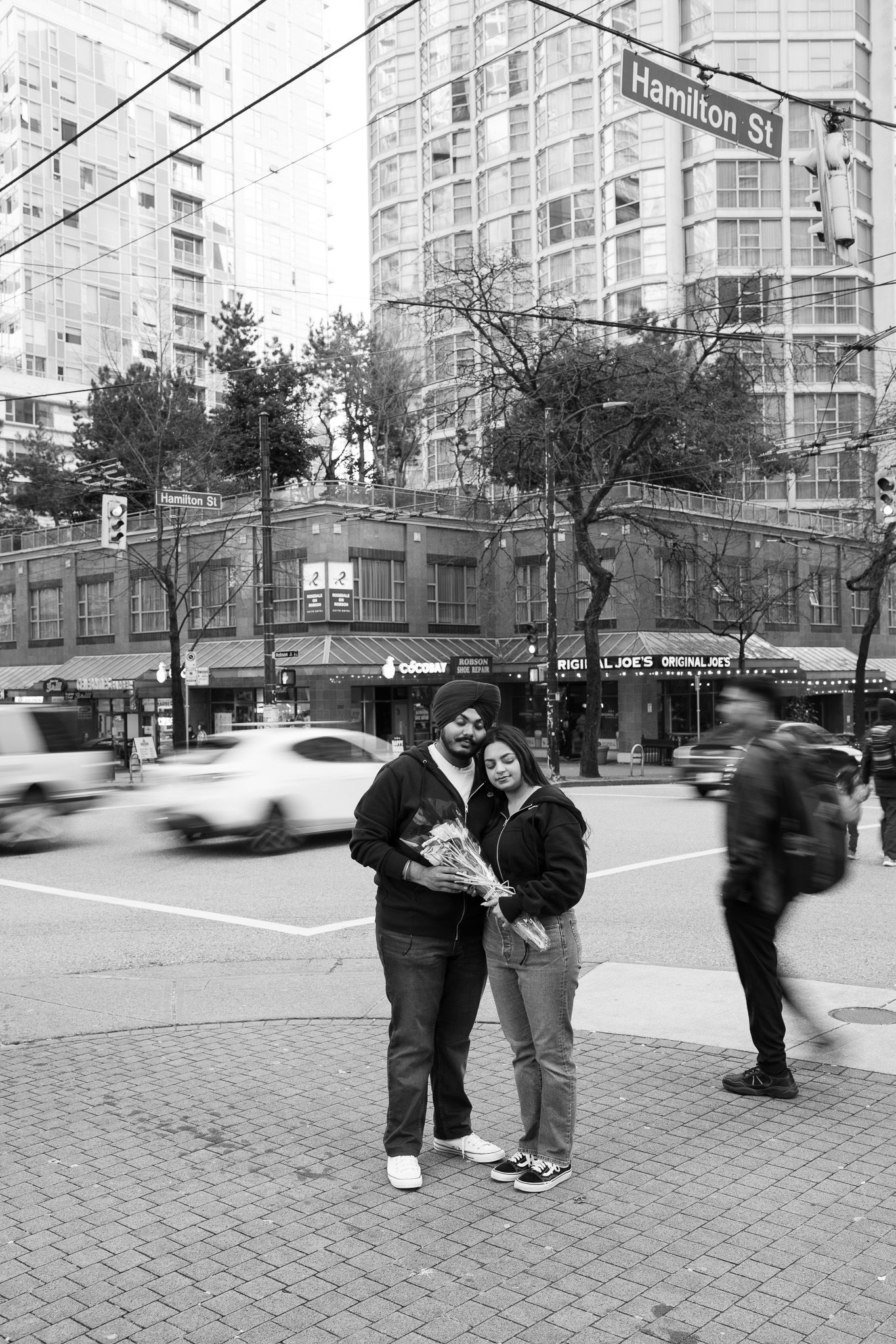 Black and white street scene in downtown Vancouver with couple standing on corner near Hamilton Street sign.