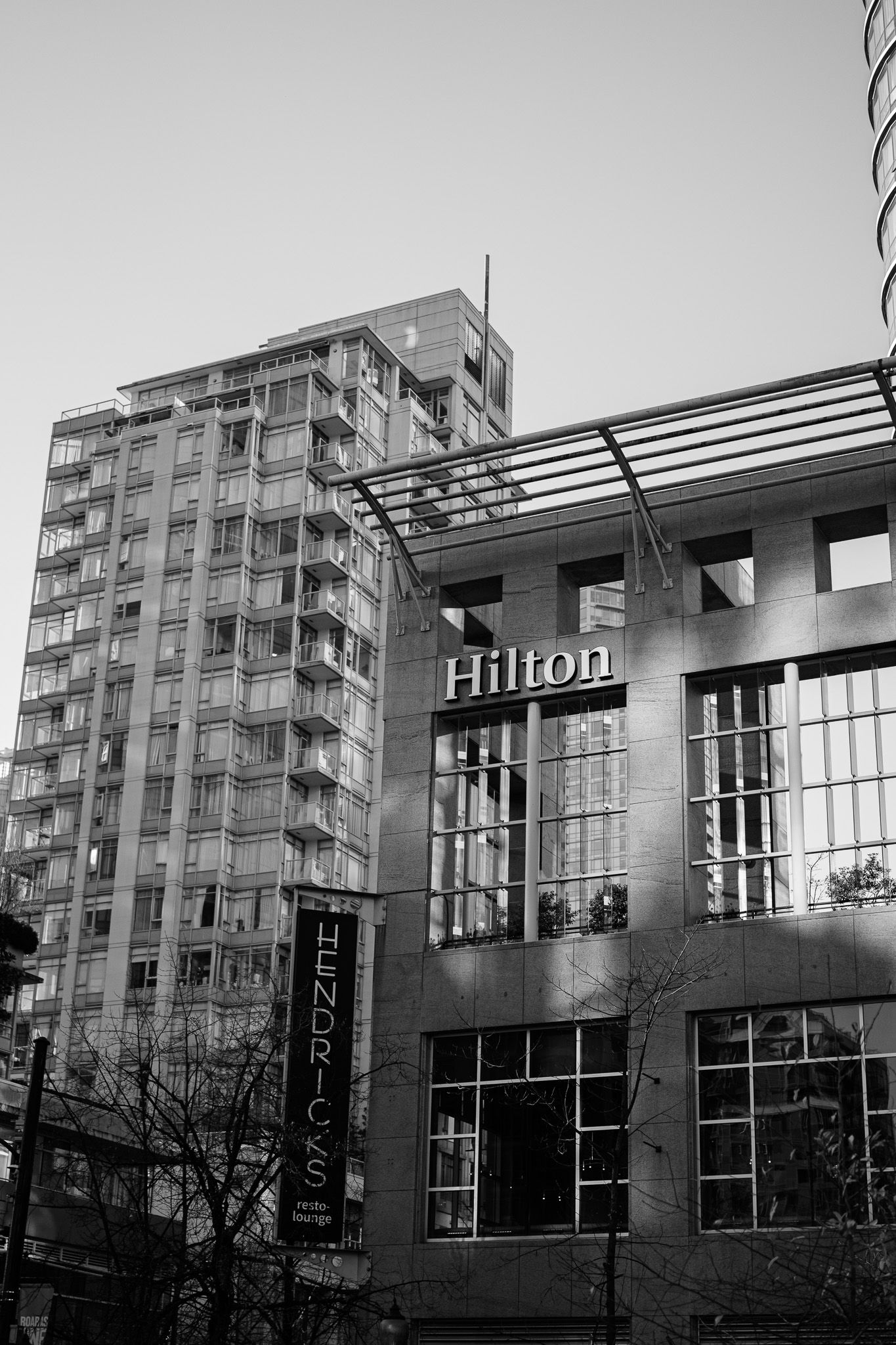 Modern glass office building with high-rise apartments visible in the background on an overcast day.