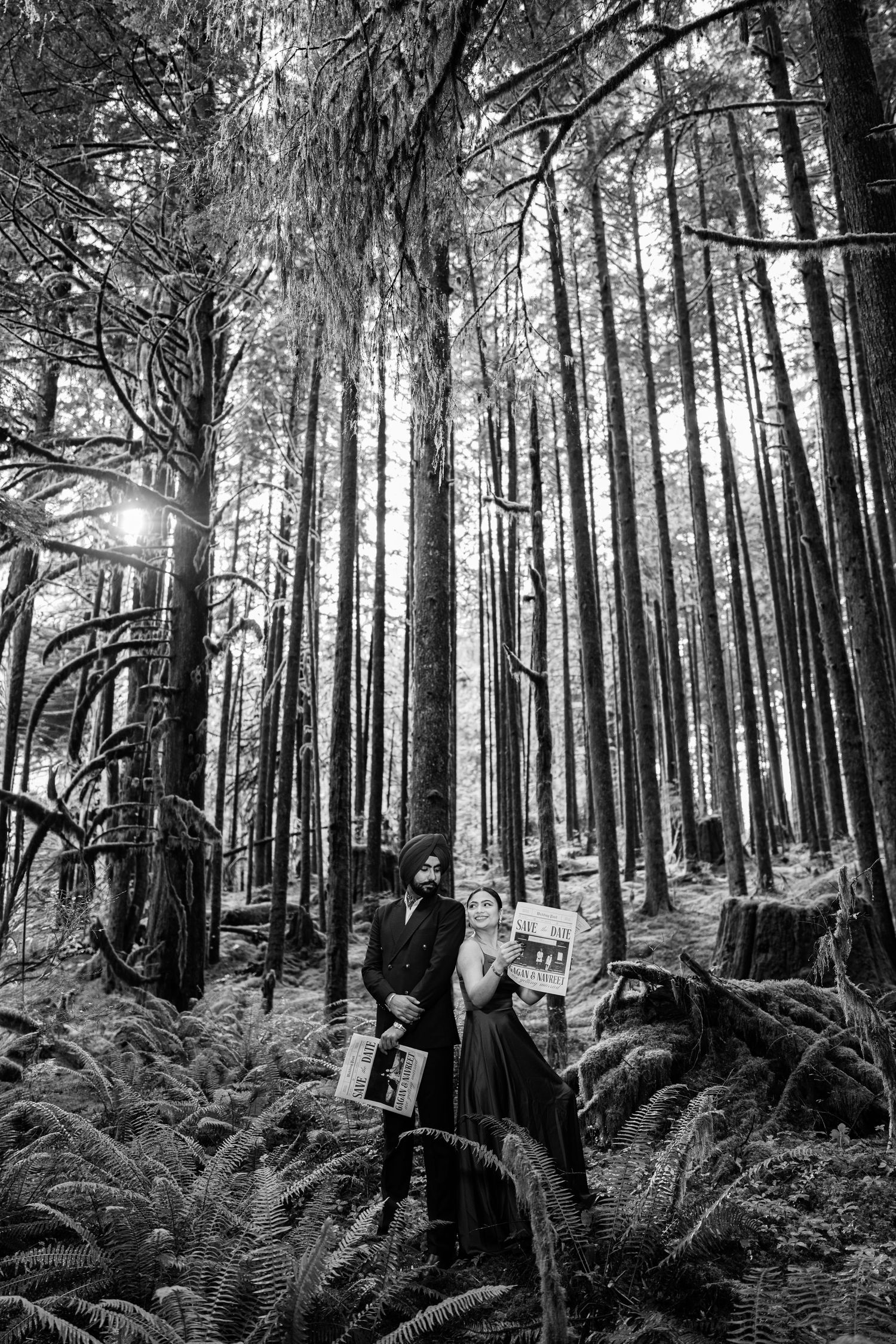 A black and white photo of a couple with newspapers among tall trees and ferns.