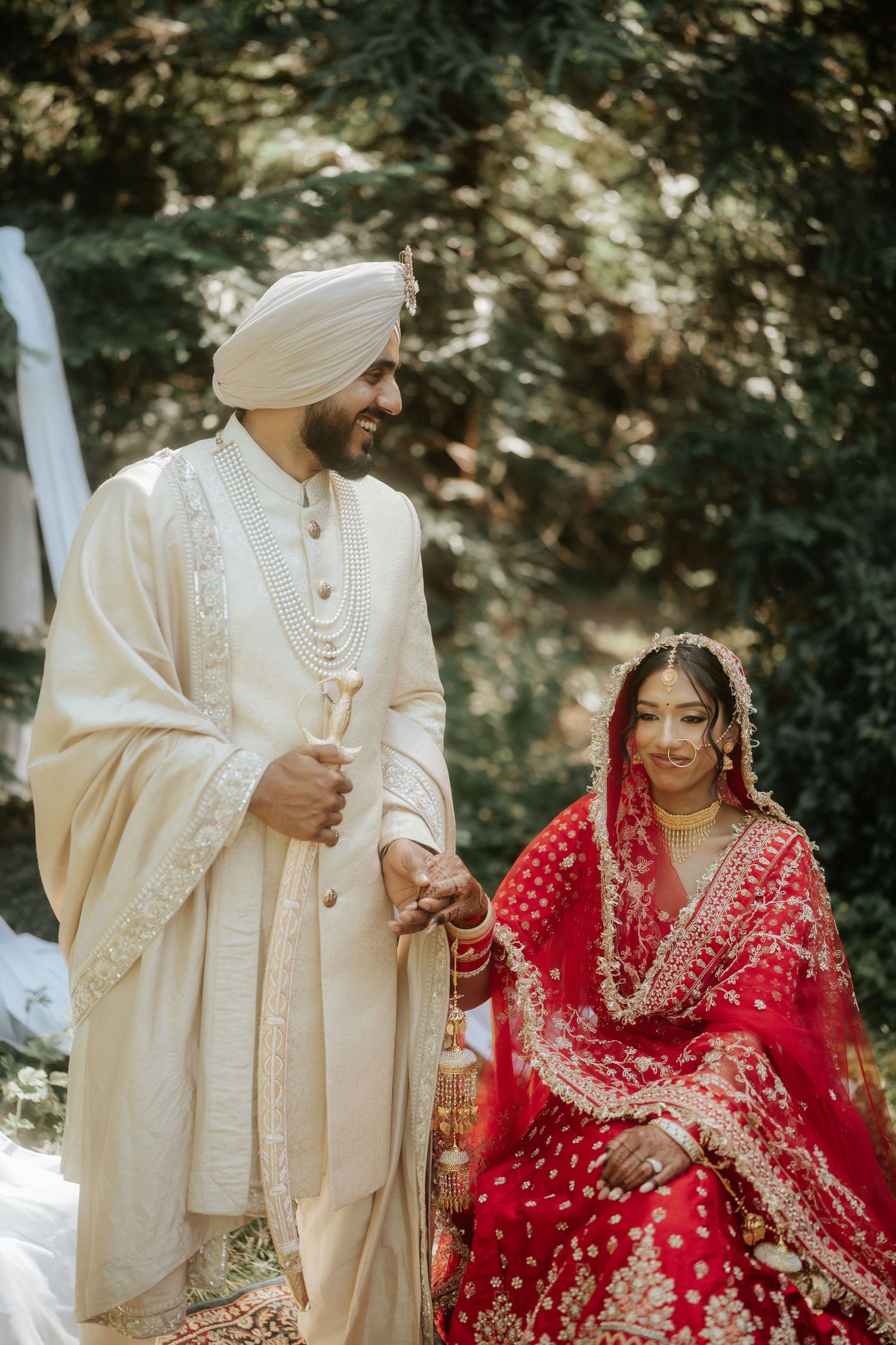 A couple in traditional Sikh wedding attire shares a moment together outdoors.