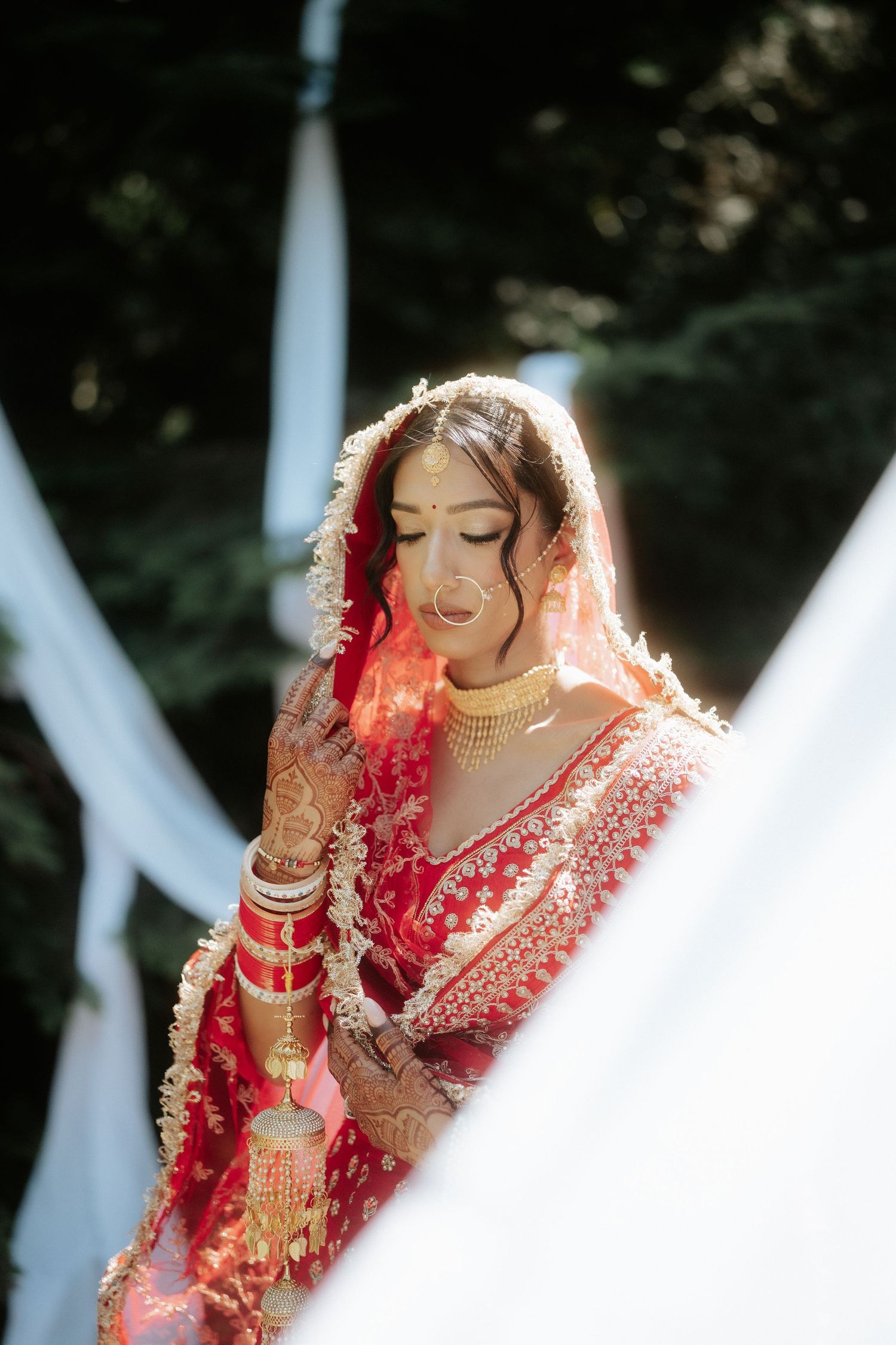 Sunlit bridal portrait featuring traditional red lehenga and delicate veil details.