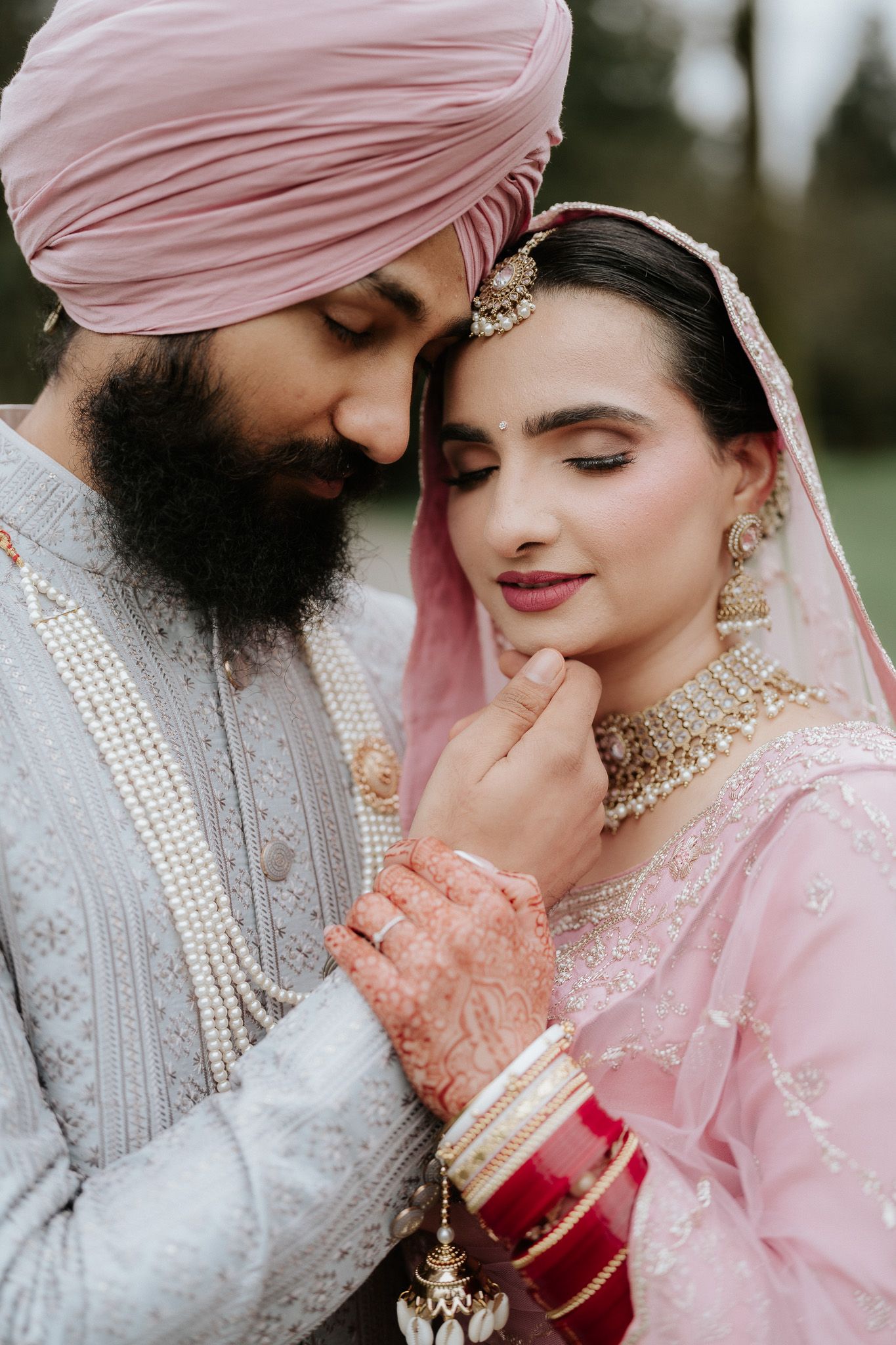 Romantic couple in traditional Sikh wedding attire share intimate moments in soft pink and pearl tones.