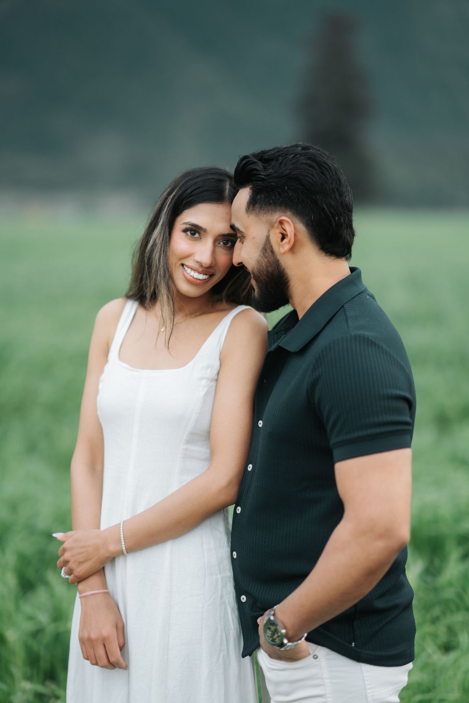 A couple shares an intimate moment in a green field, with the woman in white and the man in black.