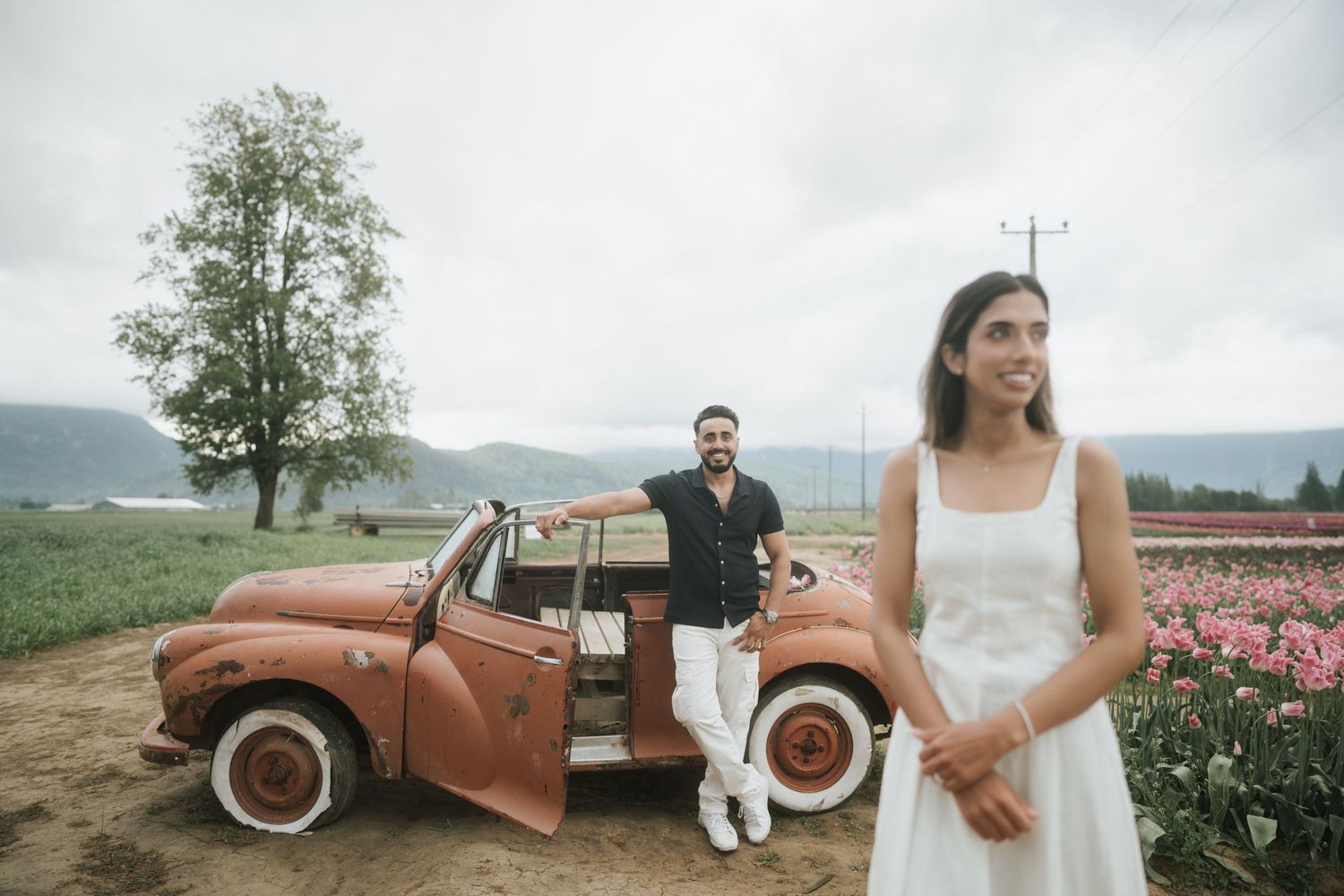 A romantic outdoor wedding photoshoot with a vintage rust-colored truck and floral backdrop in a mountainous setting.