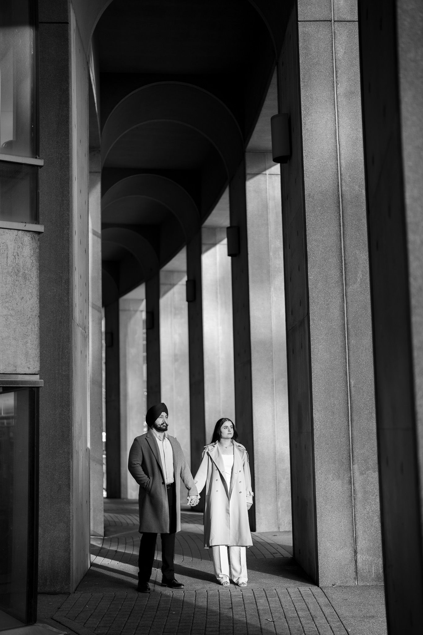 Black and white architectural photograph showing people walking through a colonnade with dramatic shadows and light.