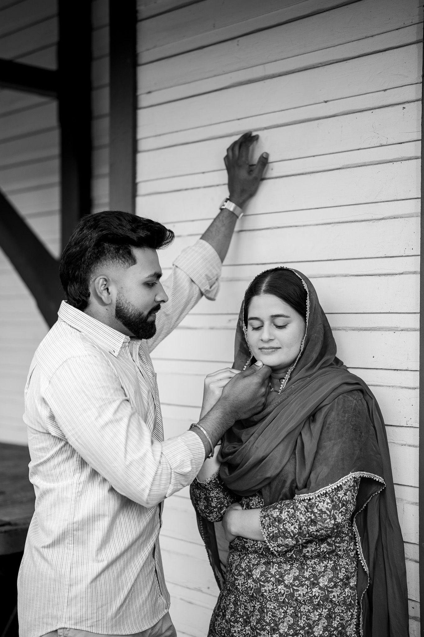 Black and white romantic photo of bearded man tenderly touching woman in traditional hijab against white wall.