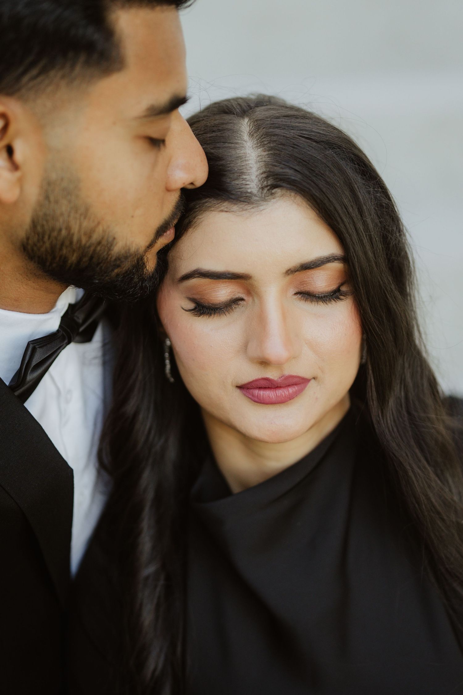 Man gently kissing woman on head as she closes her eyes in a tender romantic moment.
