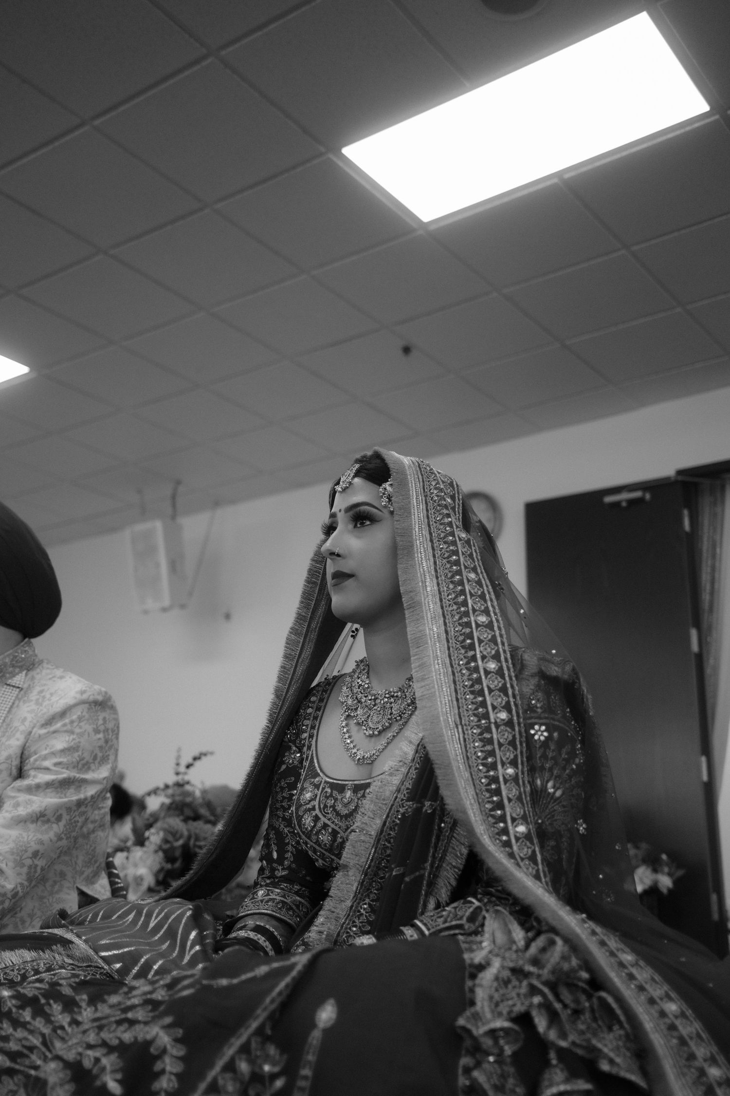 Black and white photo of a bride in traditional South Asian bridal attire with ornate jewelry and dupatta.