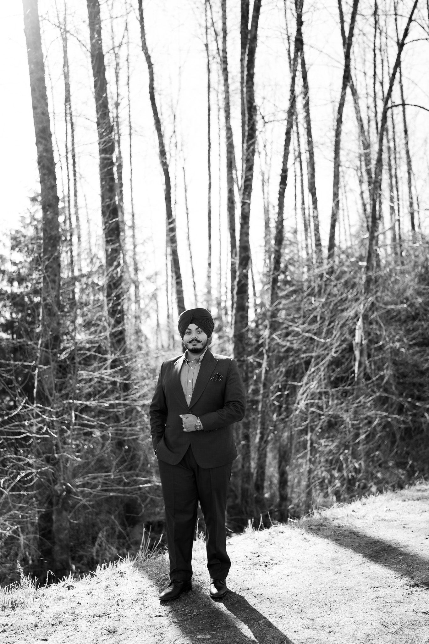 A person in a dark suit stands in a snowy winter forest setting creating a dramatic black and white scene.