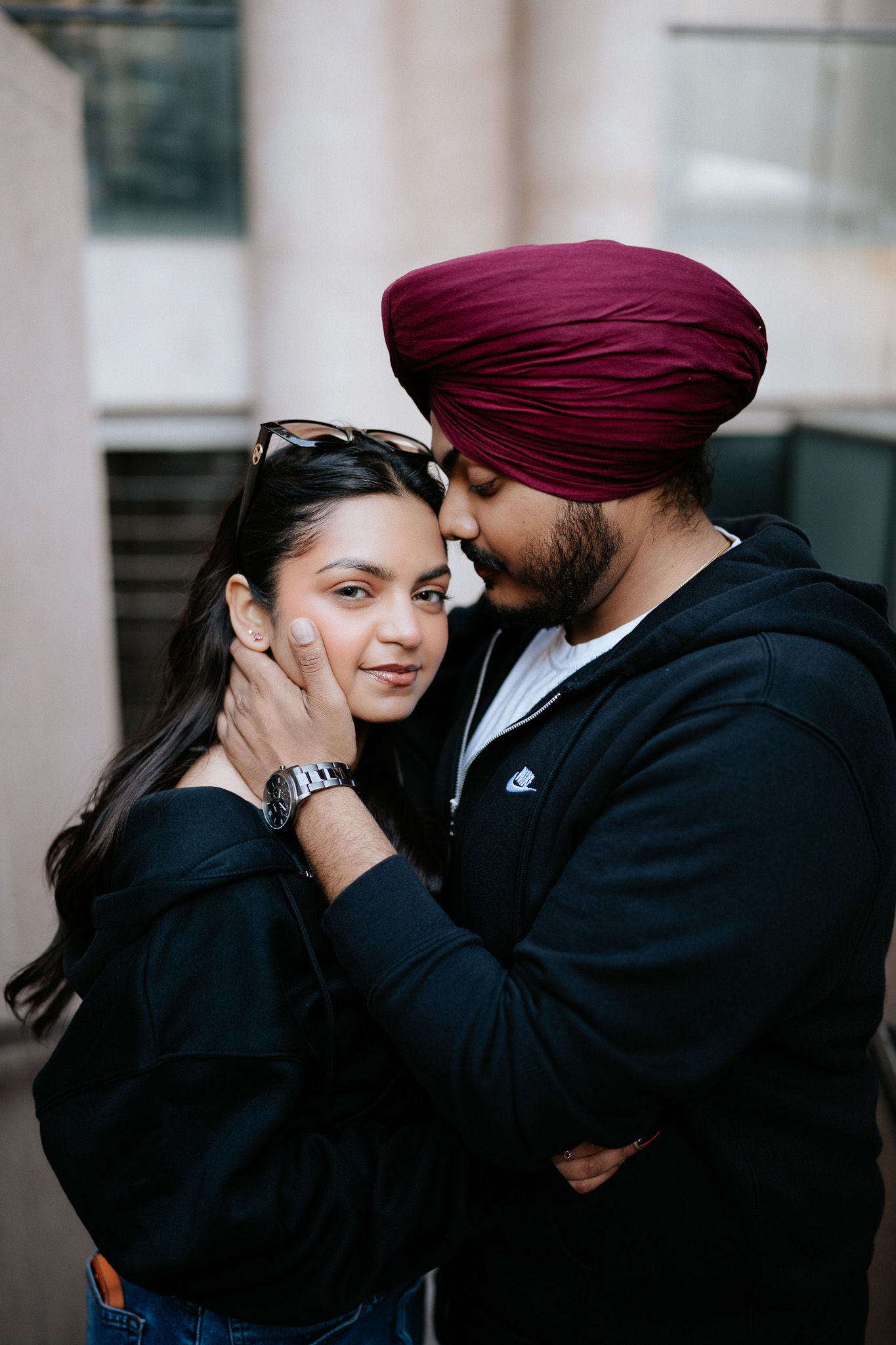 A couple in traditional attire share an intimate moment against a modern urban backdrop.
