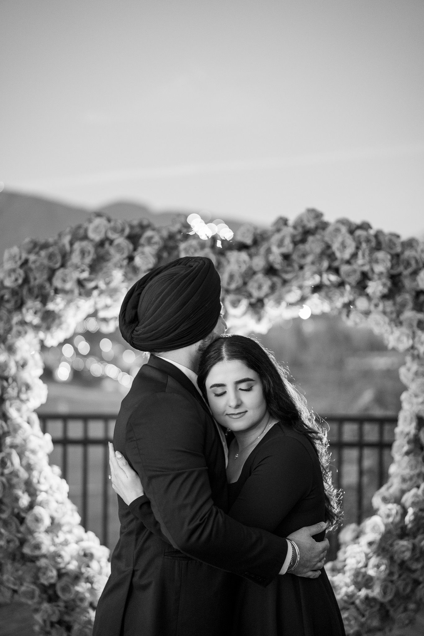 Black and white photo series showing an intimate moment between two people against a floral arch backdrop.