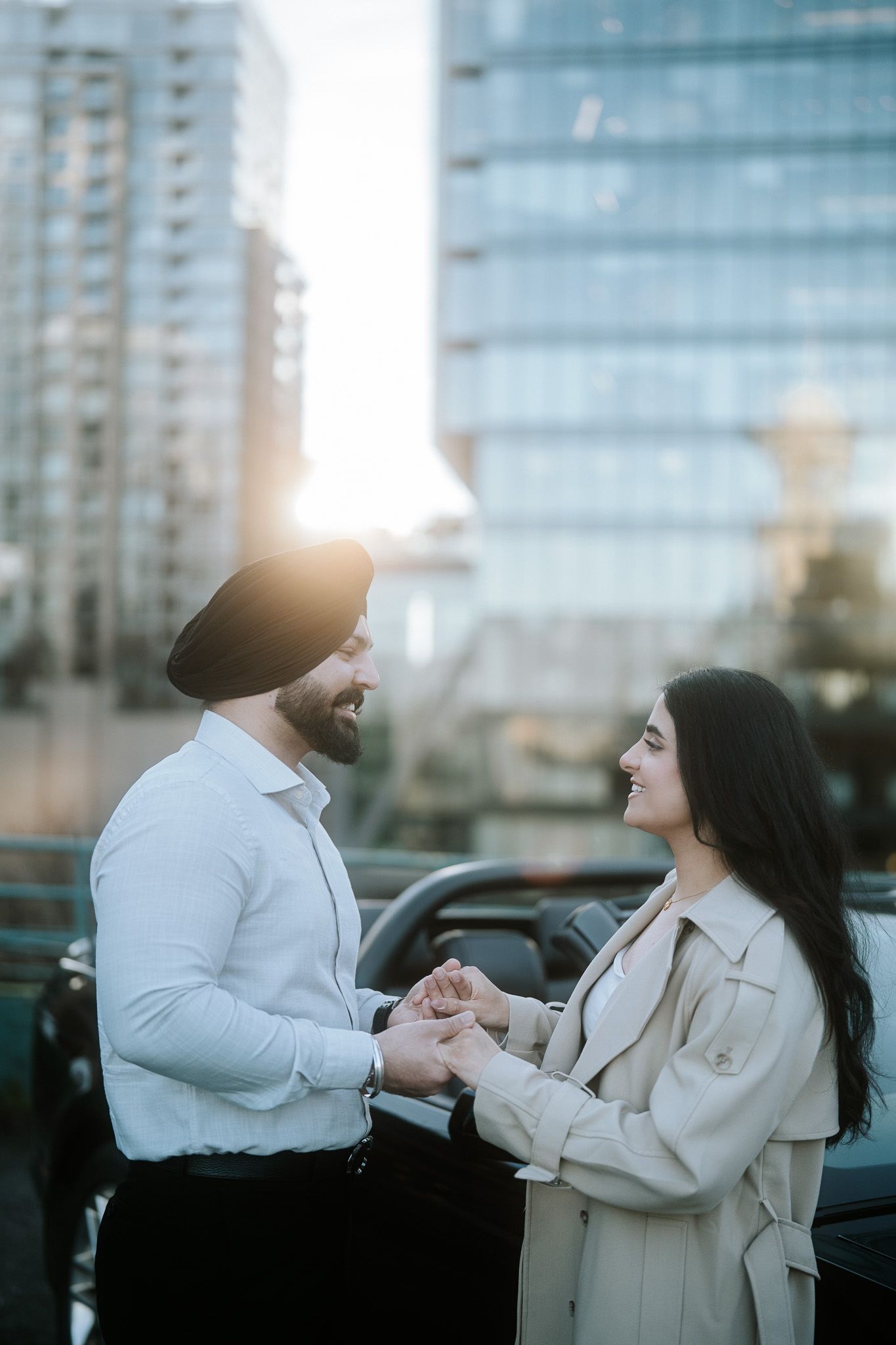 A couple shares a romantic moment during sunset against a cityscape backdrop with glass buildings.