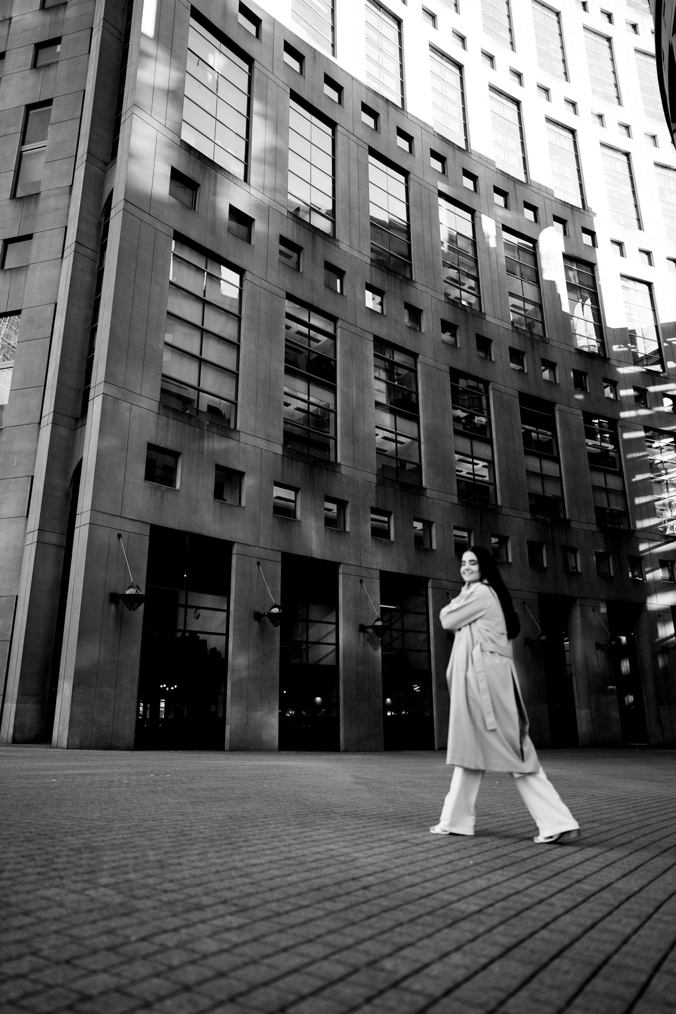 A black and white sequence of figures walking past a modern architectural facade with dramatic angular shadows.
