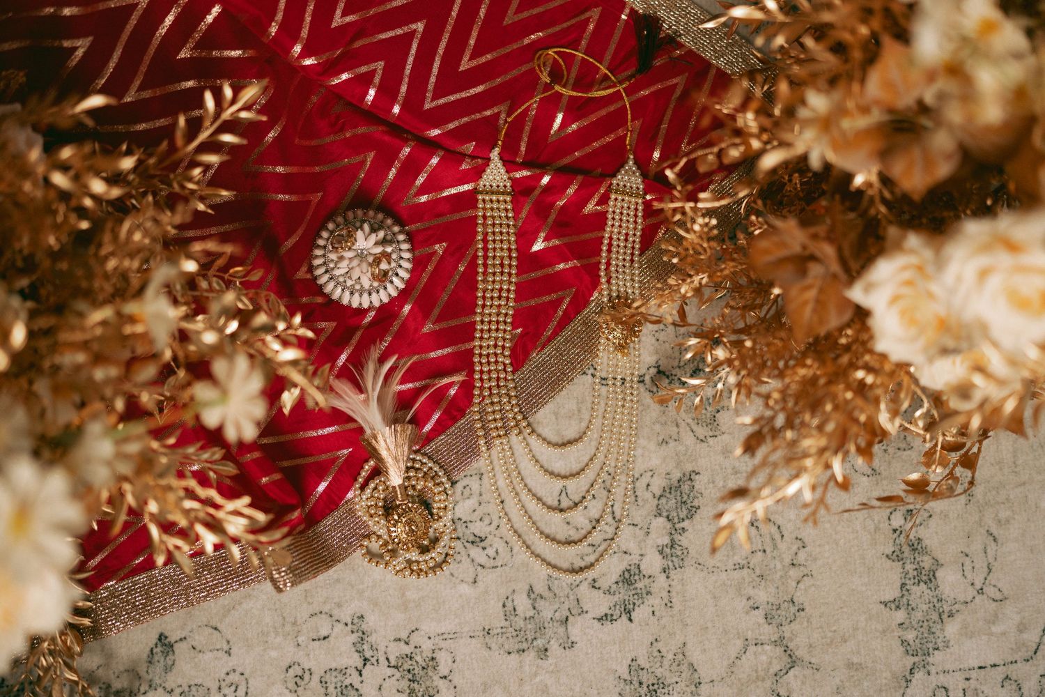 Elegant gold bridal jewelry with pearl necklace and earrings on red fabric with golden floral decor.