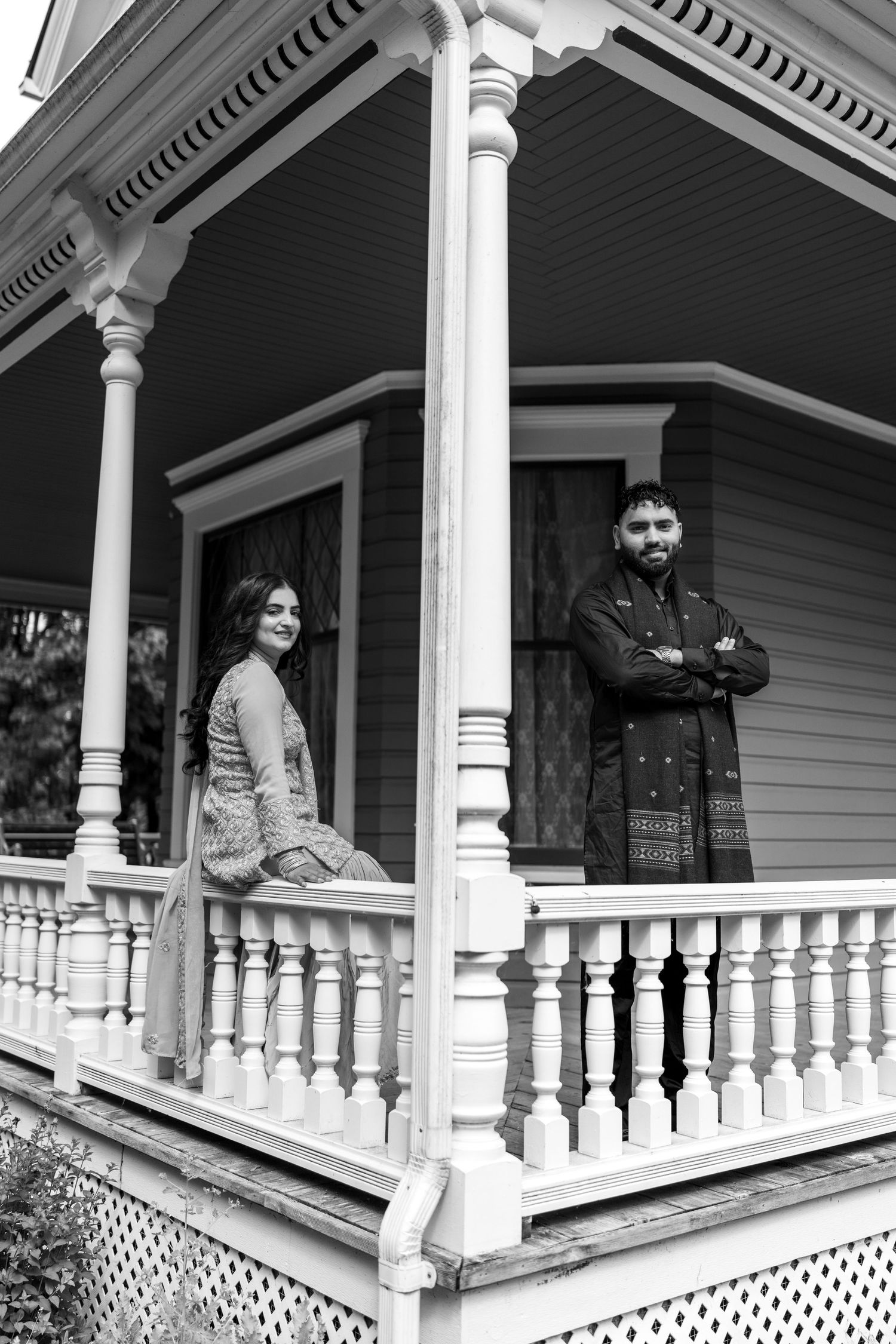Black and white photo of a Victorian porch with white columns and ornate railings.