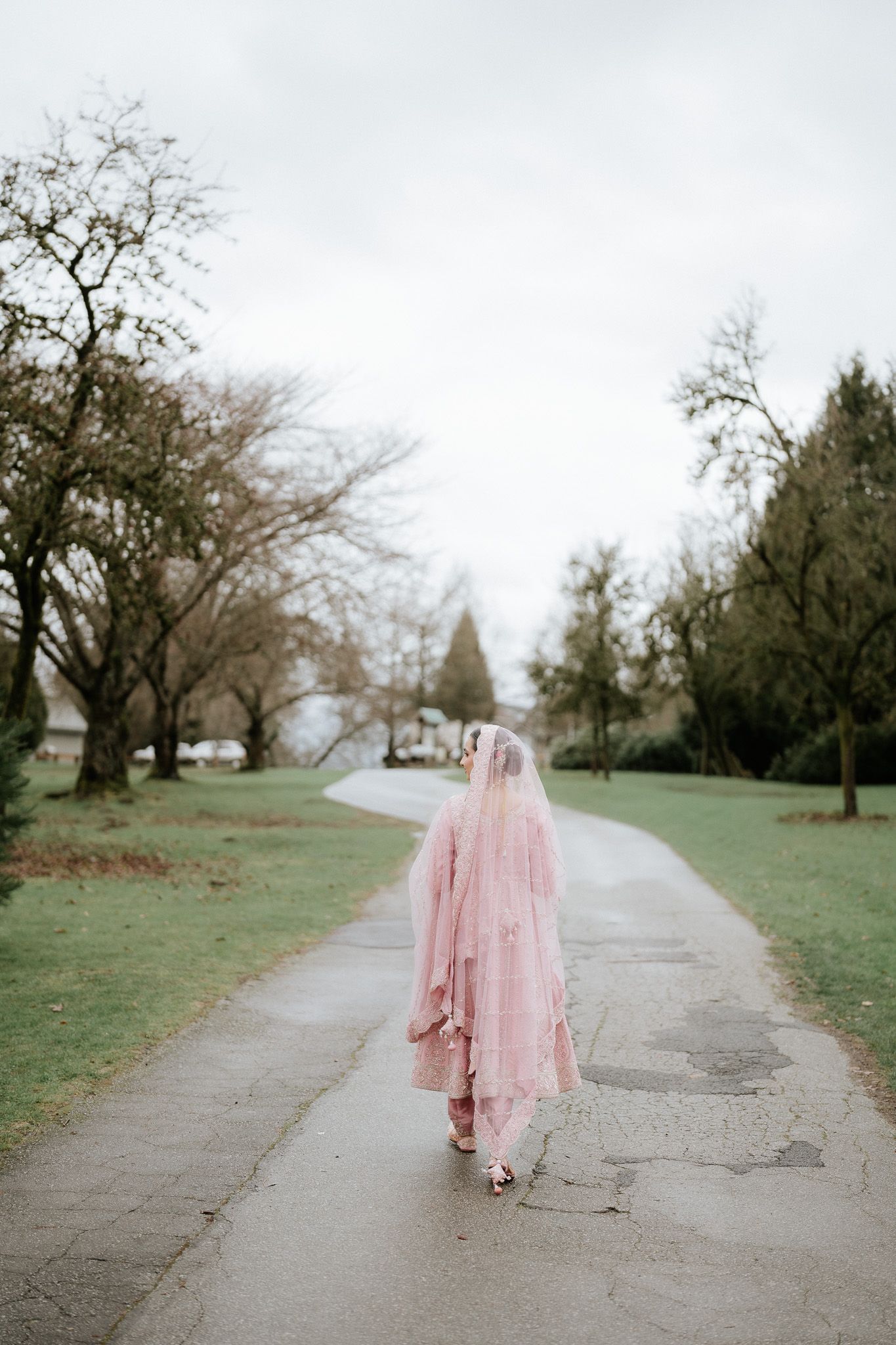 A figure in a flowing pink dress walks along a concrete path through a serene park setting.